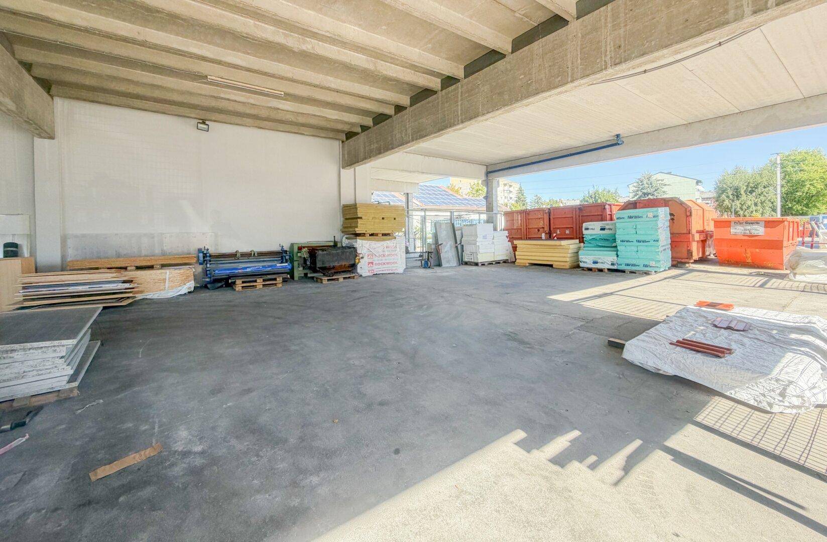 Große, helle Lagerhalle mit Betonboden und gestapelten Baumaterialien.