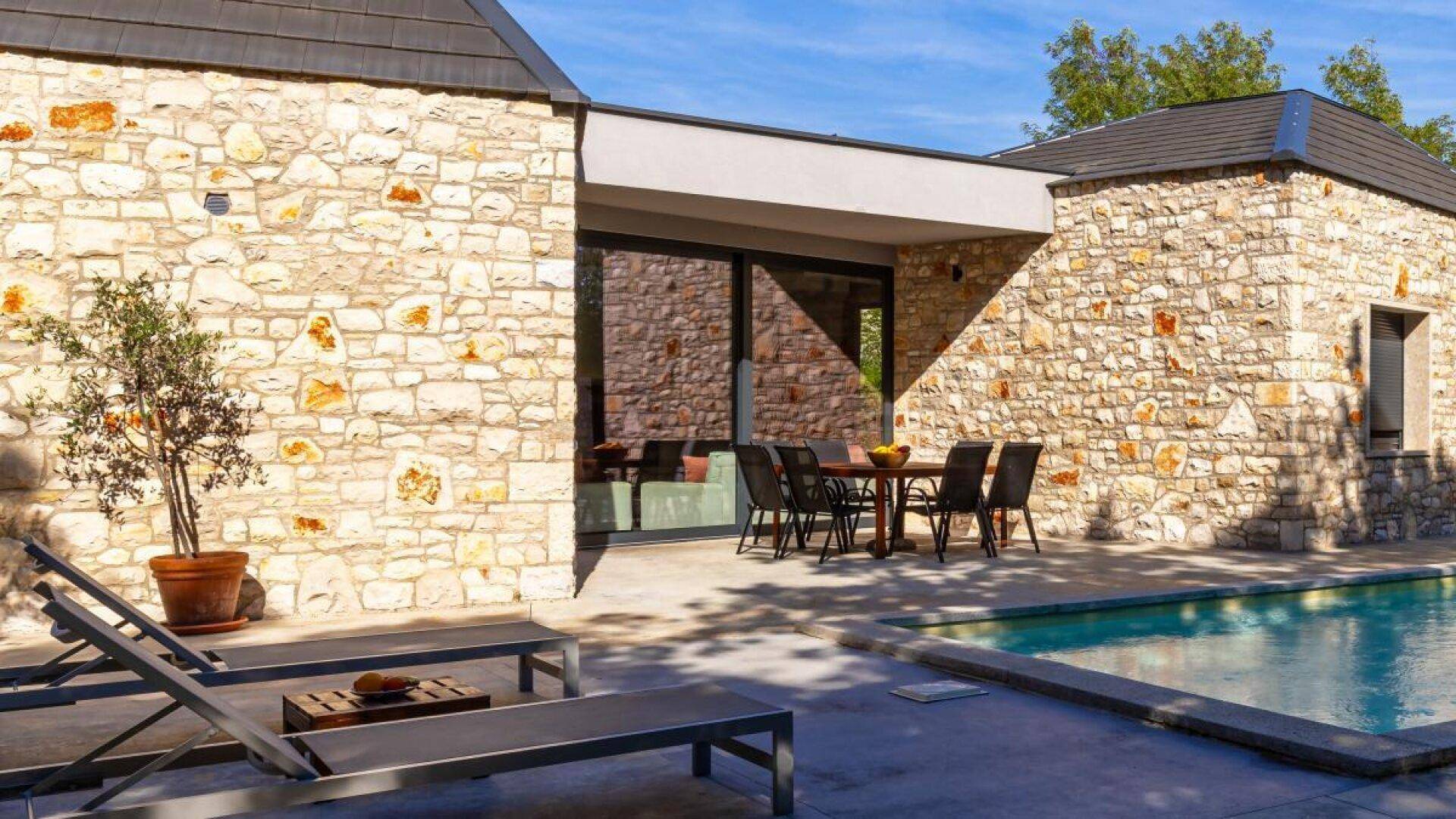 Terrasse mit Esstisch und Stühlen neben dem Pool, umgeben von der Steinfassade der Villa.