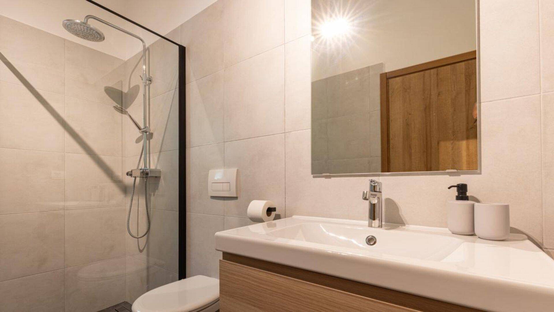 Helles Badezimmer mit Waschtisch, Spiegel und moderner Dusche mit Glasabtrennung.