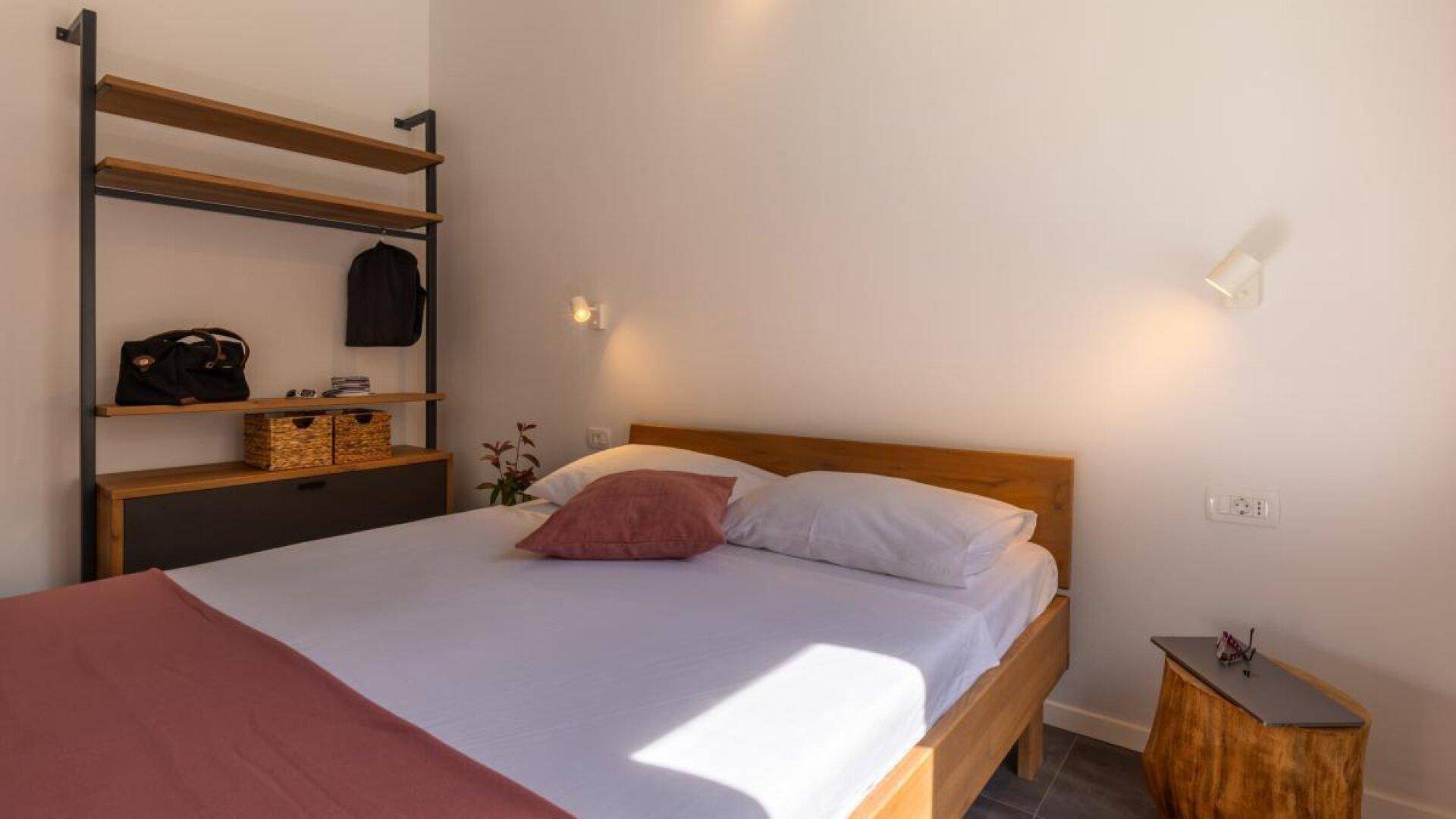 Schlafzimmer mit Holzbett, offenem Regal und hellem Ambiente durch natürliches Licht.