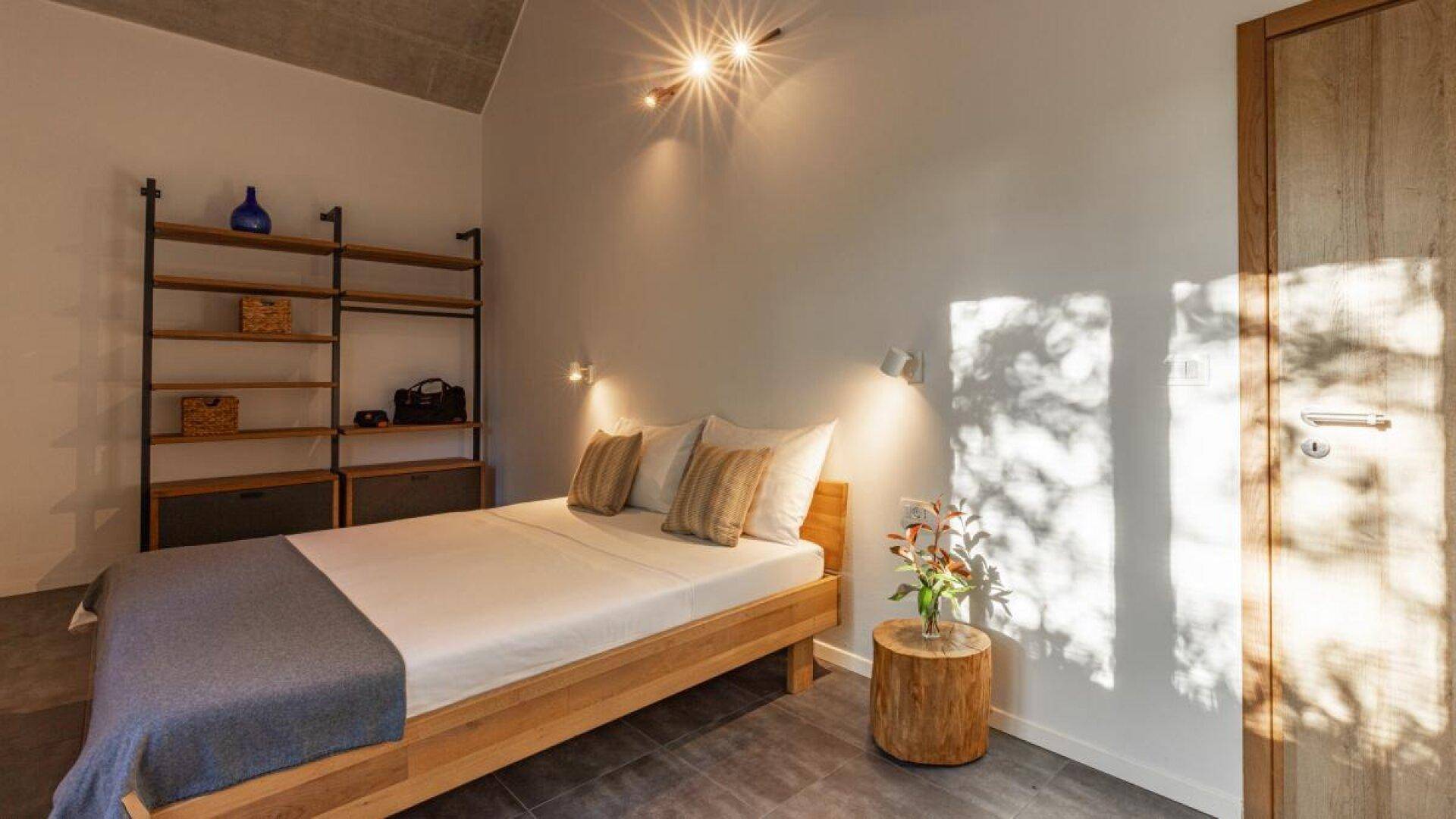 Gemütliches Schlafzimmer mit Holzbett, offenem Regal und natürlichem Lichteinfall durch die Tür.