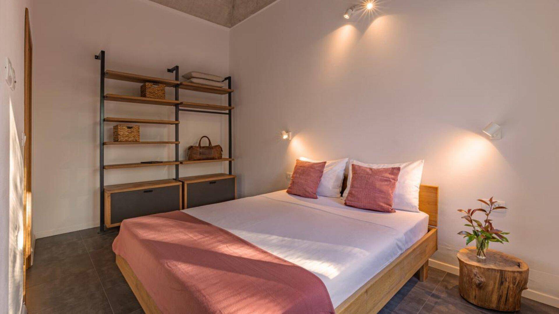Helles Schlafzimmer mit Holzbett, offenem Regal und indirekter Beleuchtung für eine gemütliche Atmosphäre.