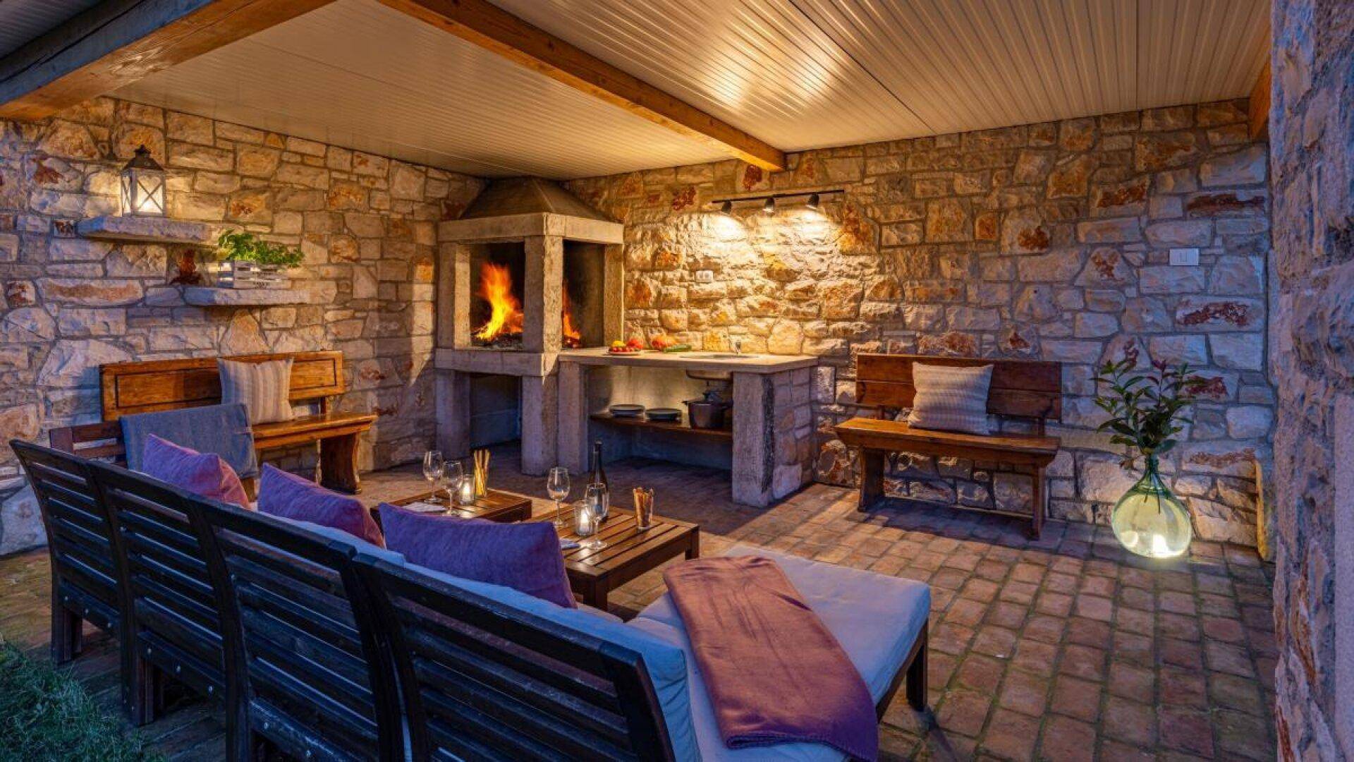 Gemütliche Steinterrasse mit Lounge-Möbeln, Kamin und integriertem Grillbereich, ideal für gesellige Stunden.