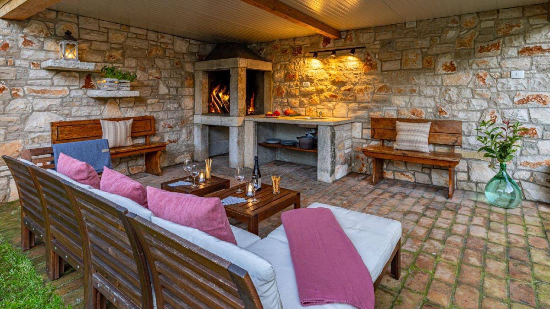 Überdachte Steinterrasse mit gemütlicher Sitzecke, Kamin und Grillbereich für entspannte Abende im Freien.