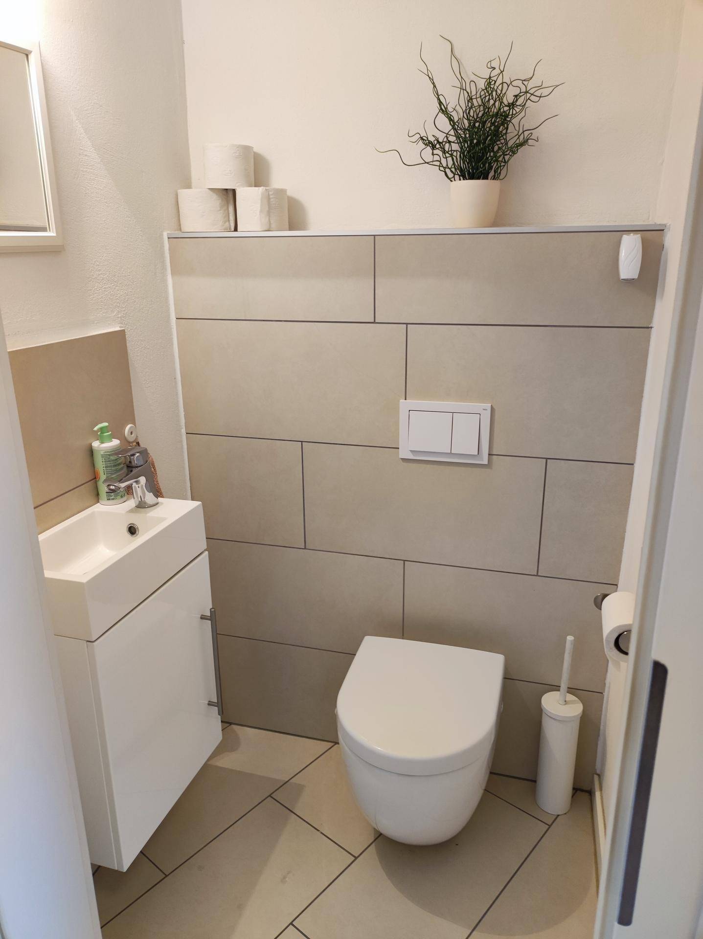 Modernes Gäste-WC mit wandhängender Toilette, kleinem Waschbecken und Fliesenboden.