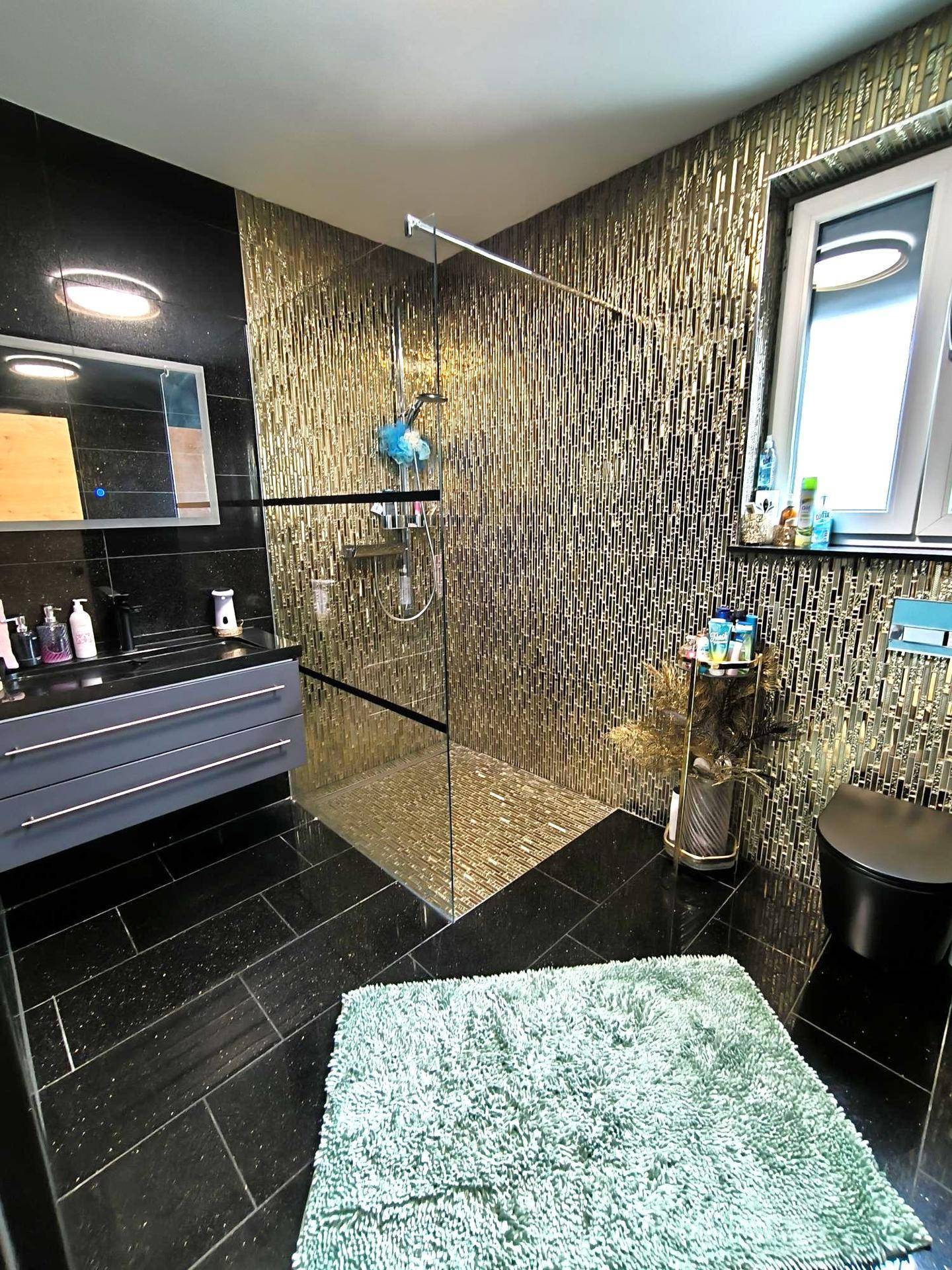 Luxuriöses Badezimmer mit goldfarbenen Mosaikfliesen, begehbarer Dusche und modernem Waschtisch.