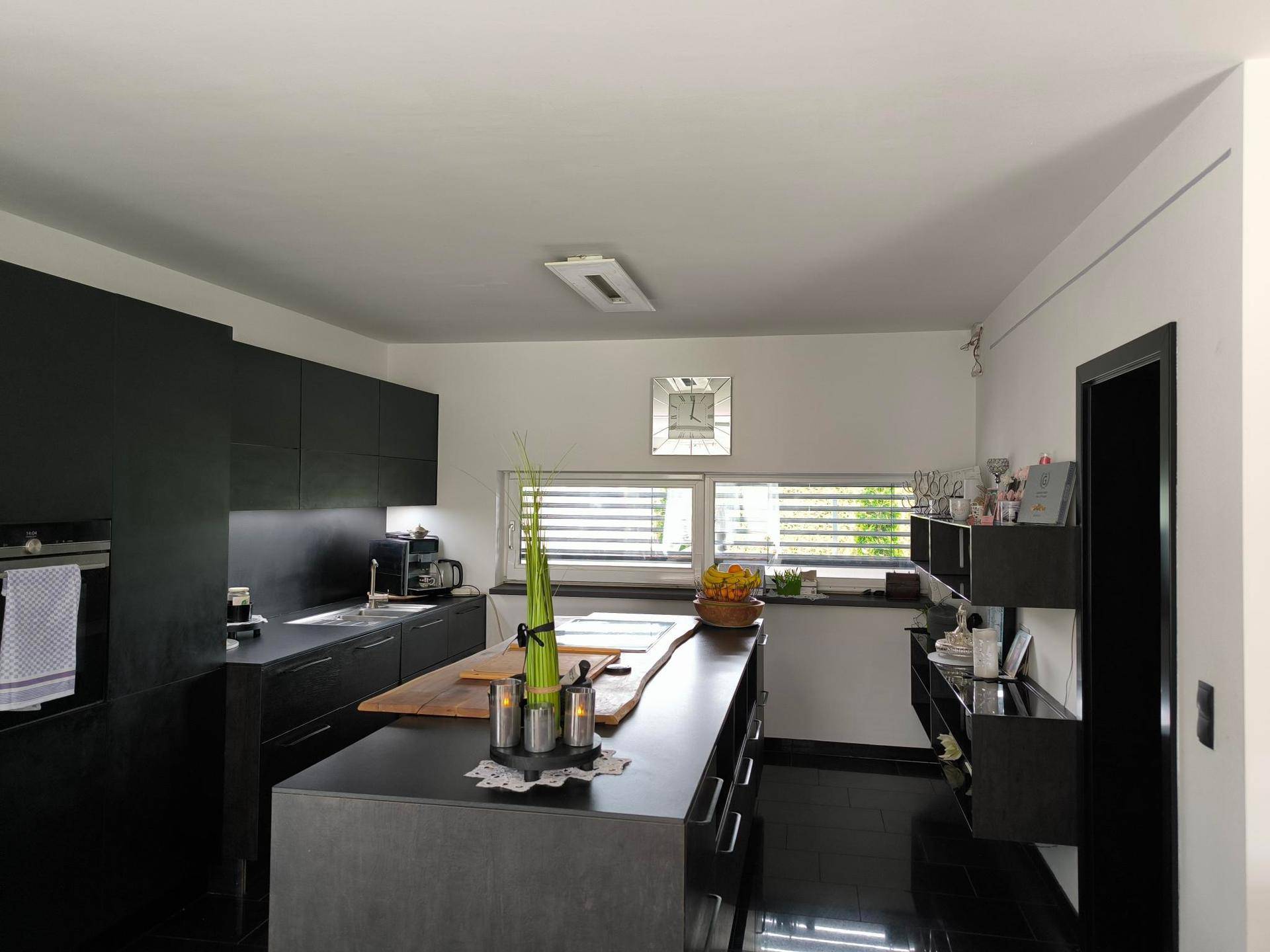 Moderne Küche mit schwarzen Schränken, Kücheninsel aus Holz und glänzenden Fliesenböden.