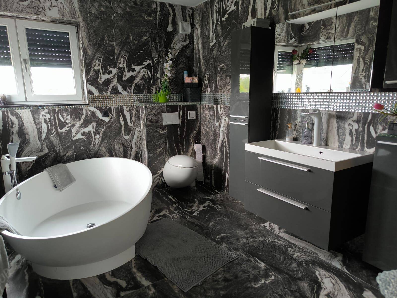 Elegantes Badezimmer mit freistehender Badewanne, Marmorfliesen und modernem Waschtisch mit Spiegelschrank.