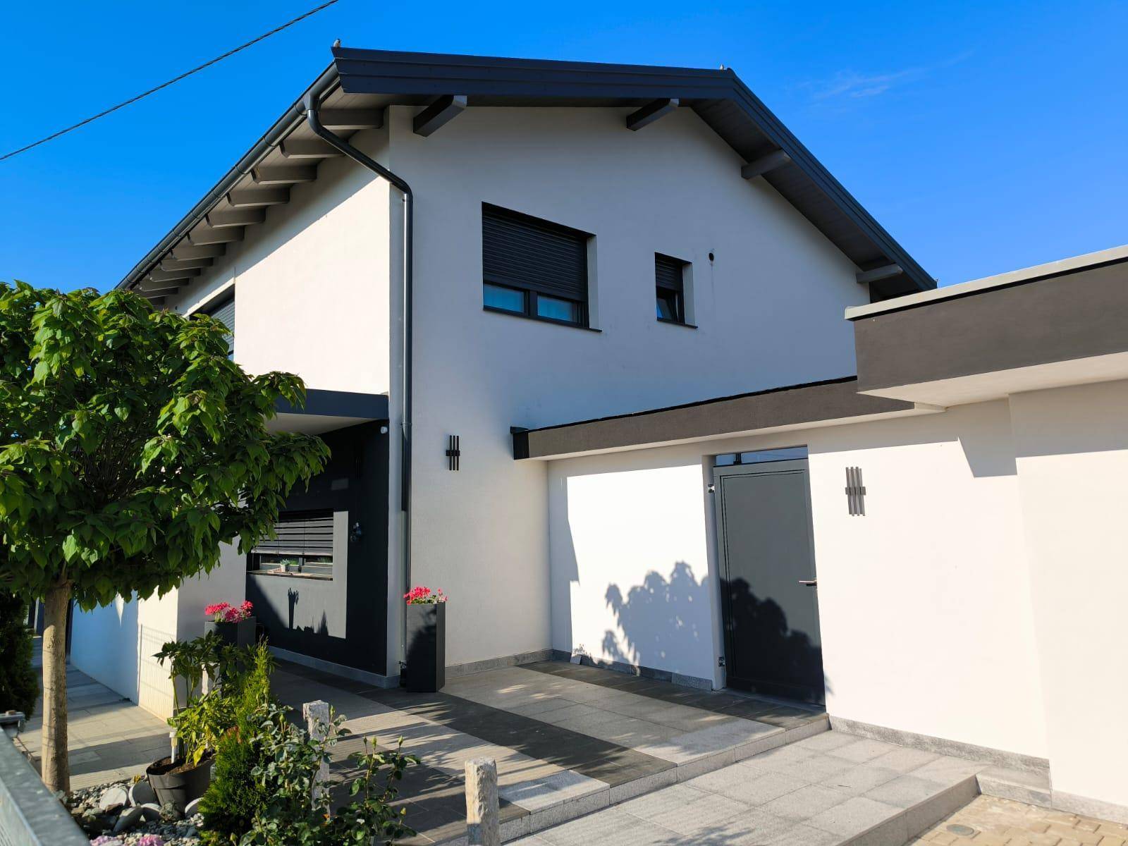 Eingangsbereich des modernen Hauses mit Vordach, weißen Wänden und dunklen Akzenten unter klarem Himmel.