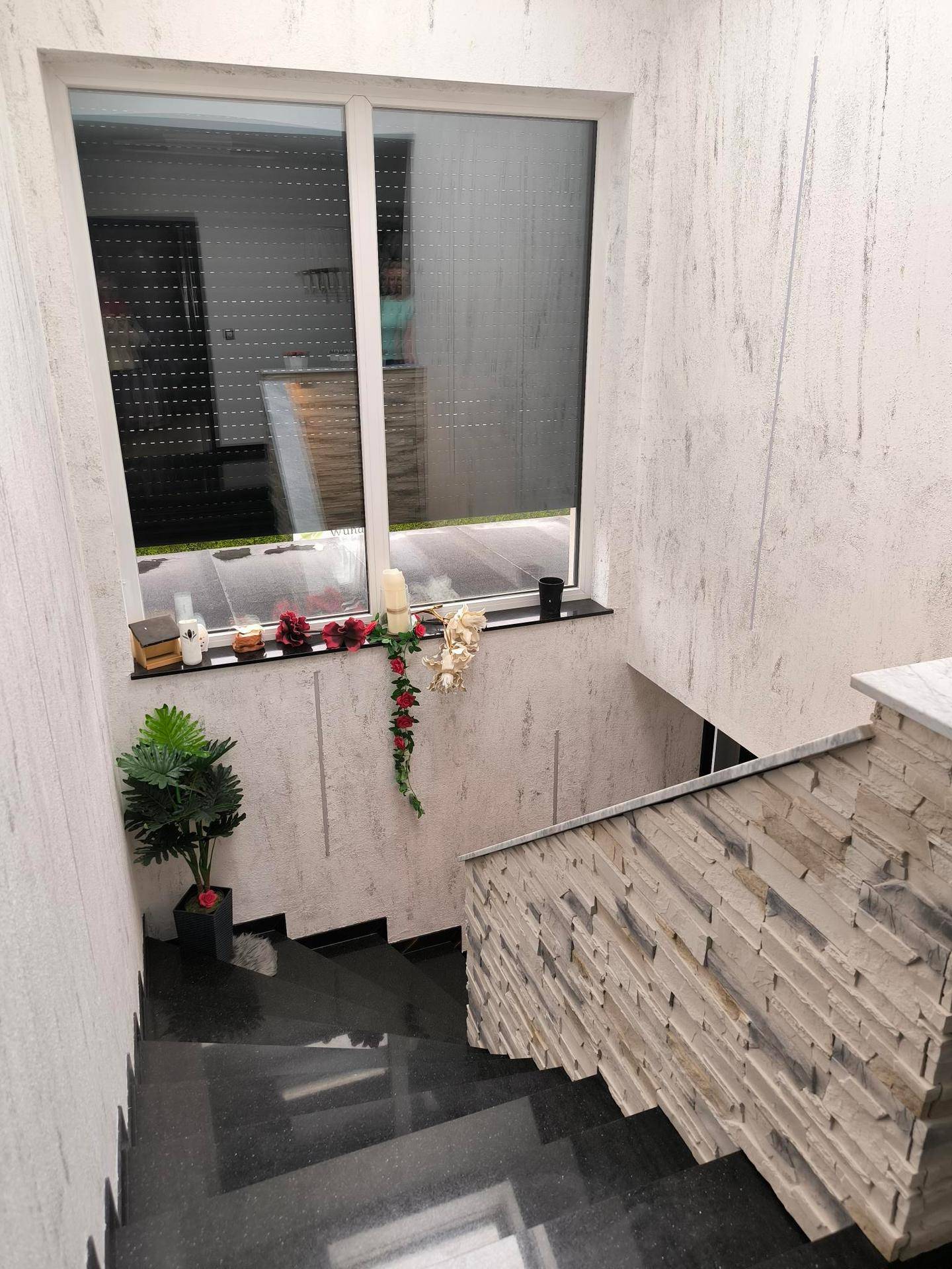 Moderner Treppenaufgang mit dunklen Granitstufen und dekorativer Steinwand, beleuchtet durch ein Fenster.