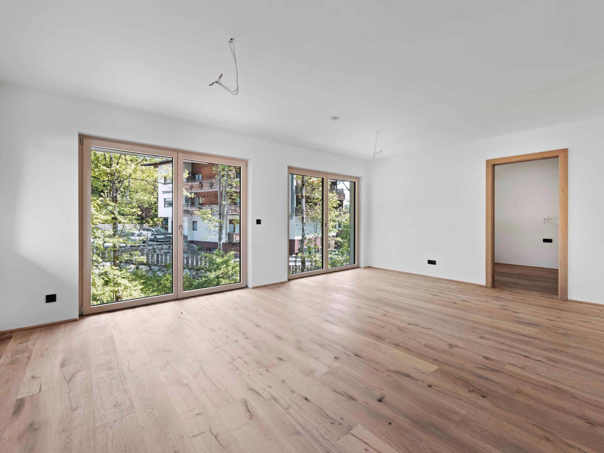 Heller, leerer Wohnraum mit Eichenparkettboden und großen Schiebetüren zum Außenbereich.