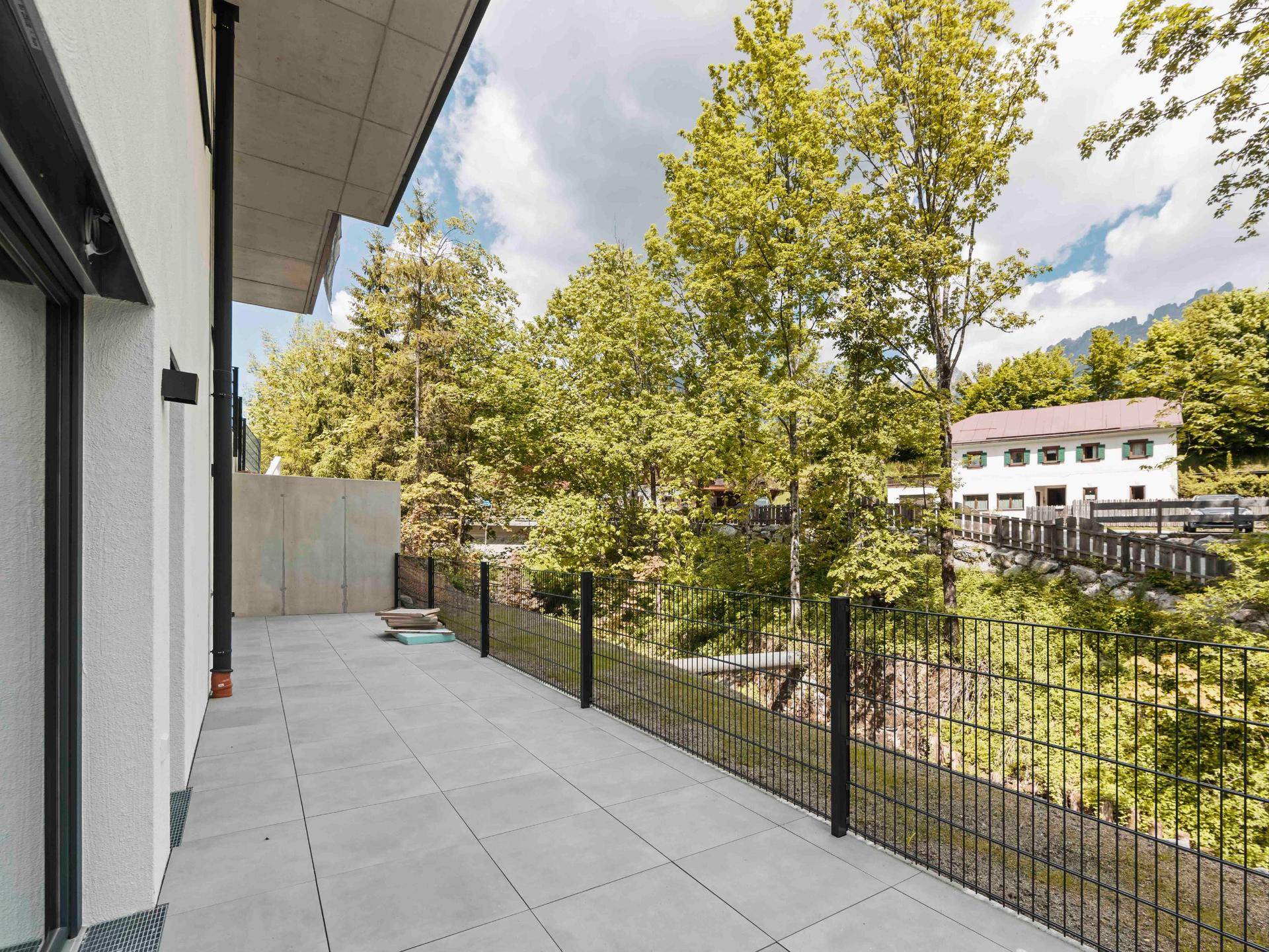 Geräumige Außenterrasse mit grauen Fliesen und Blick ins Grüne, umgeben von Bäumen.