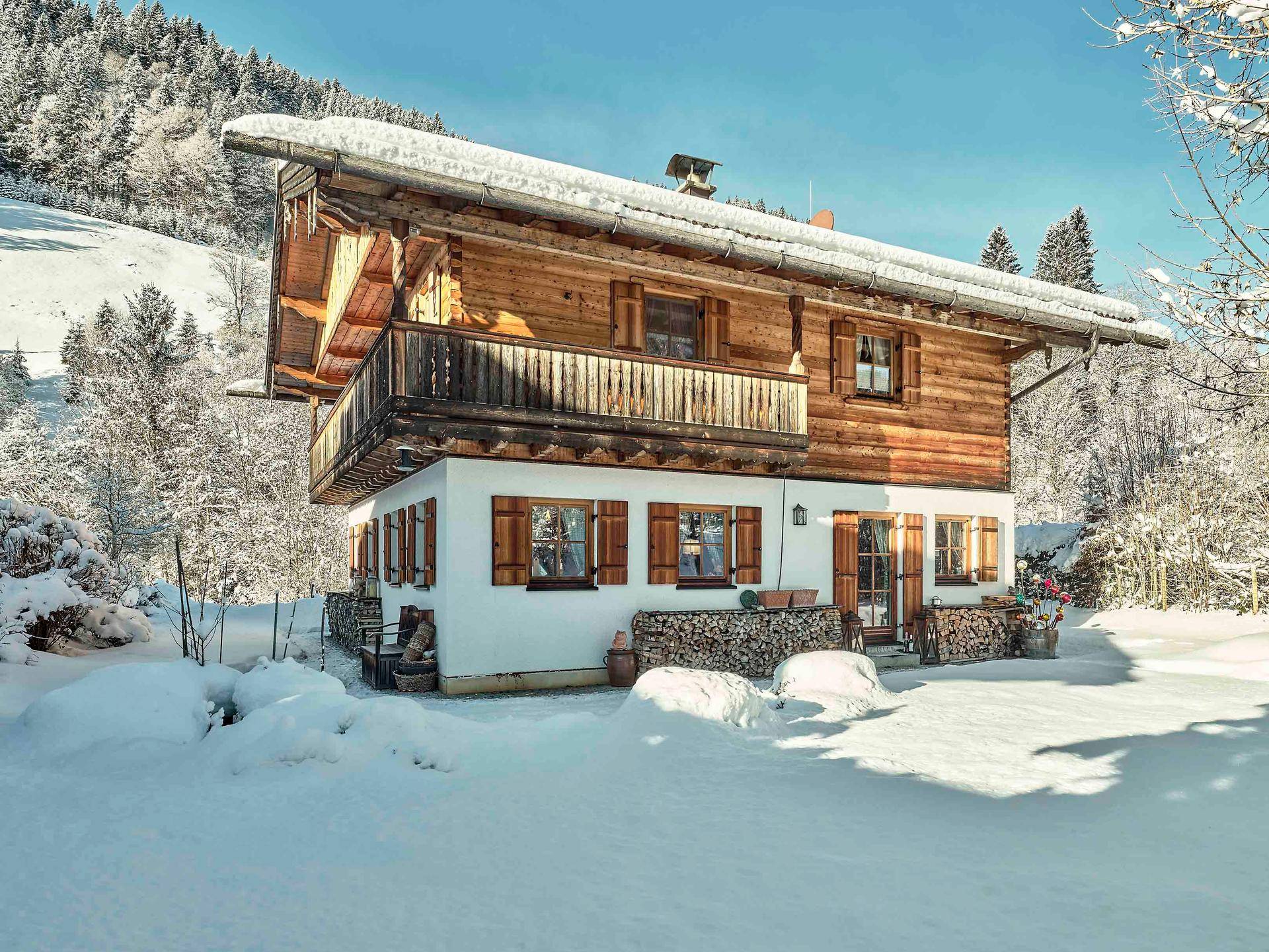 Charmantes Holzhaus im Schnee, umgeben von Bäumen und mit einem Balkon im Obergeschoss.