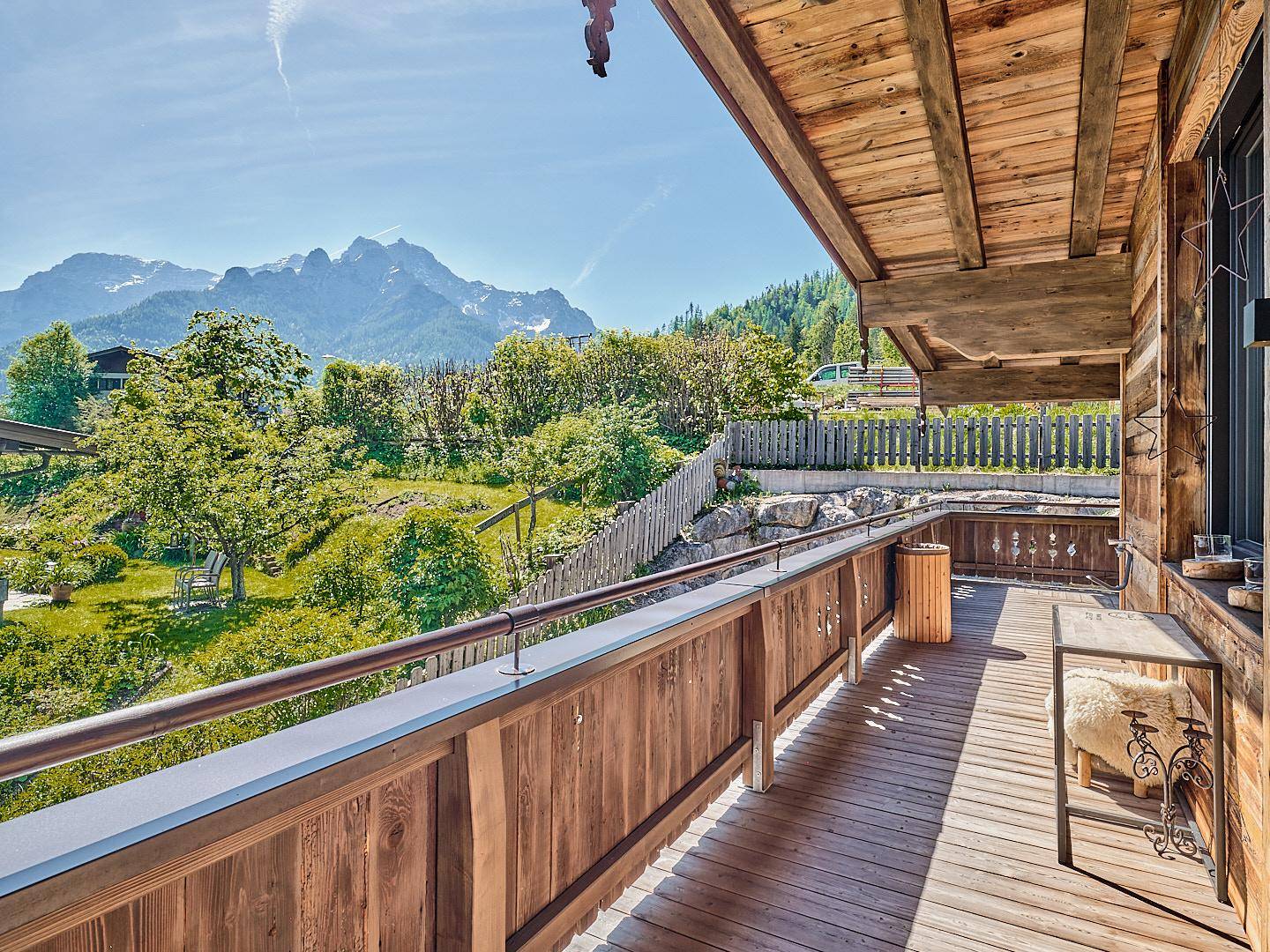 Sonniger Holzbalkon mit Blick auf die umliegende grüne Landschaft und majestätische Berge.