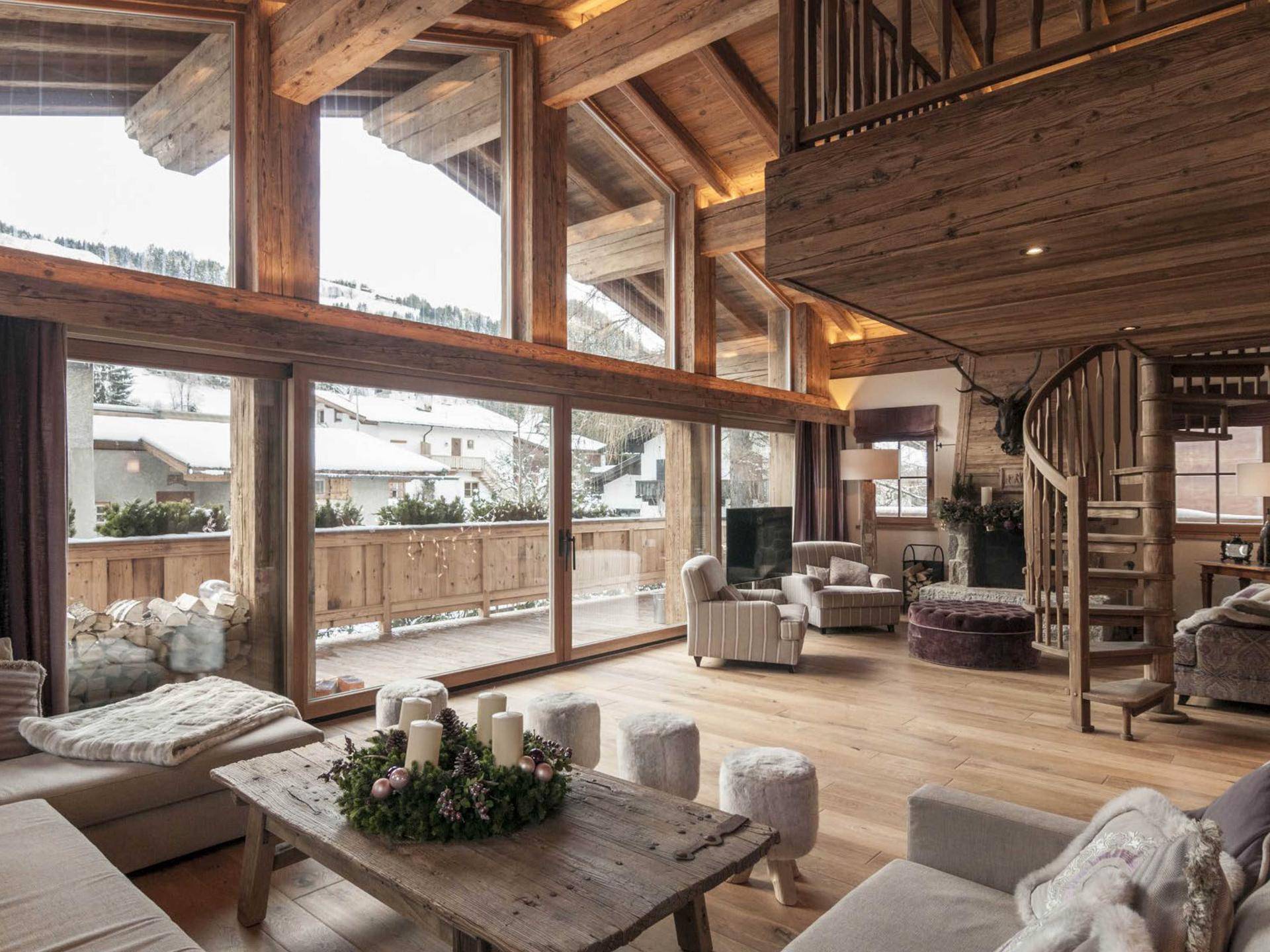 Geräumiges Wohnzimmer im Chalet-Stil mit hohen Decken, Holzbalken und großen Fenstern mit Bergblick.