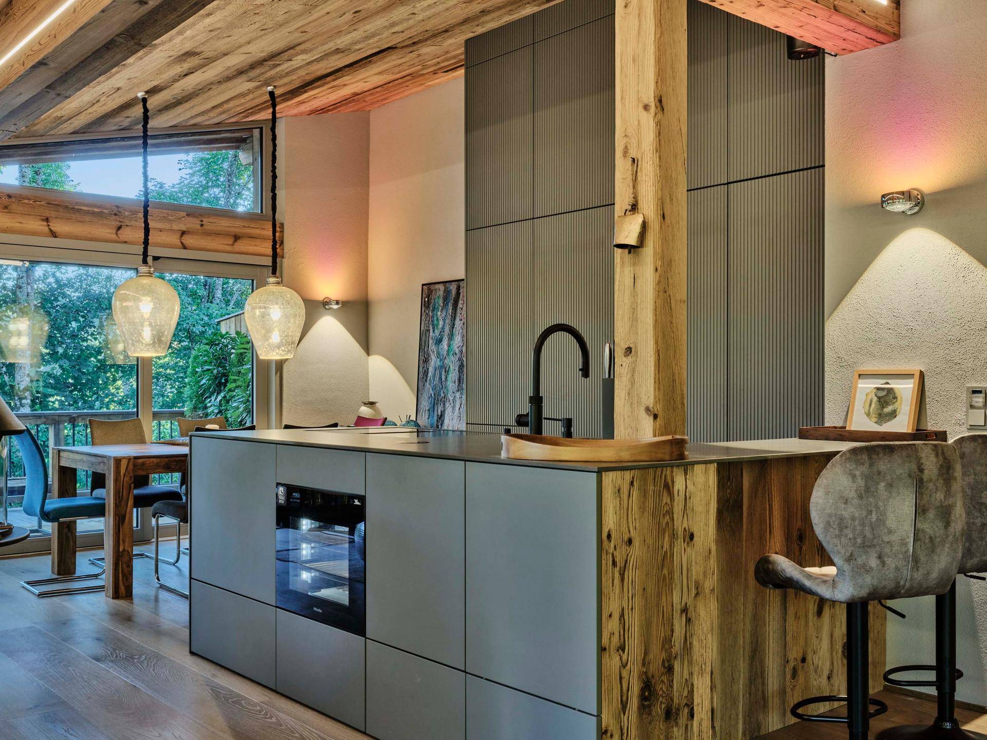 Moderne Küche mit Kücheninsel, integriertem Backofen und Holzelementen im offenen Wohnbereich.