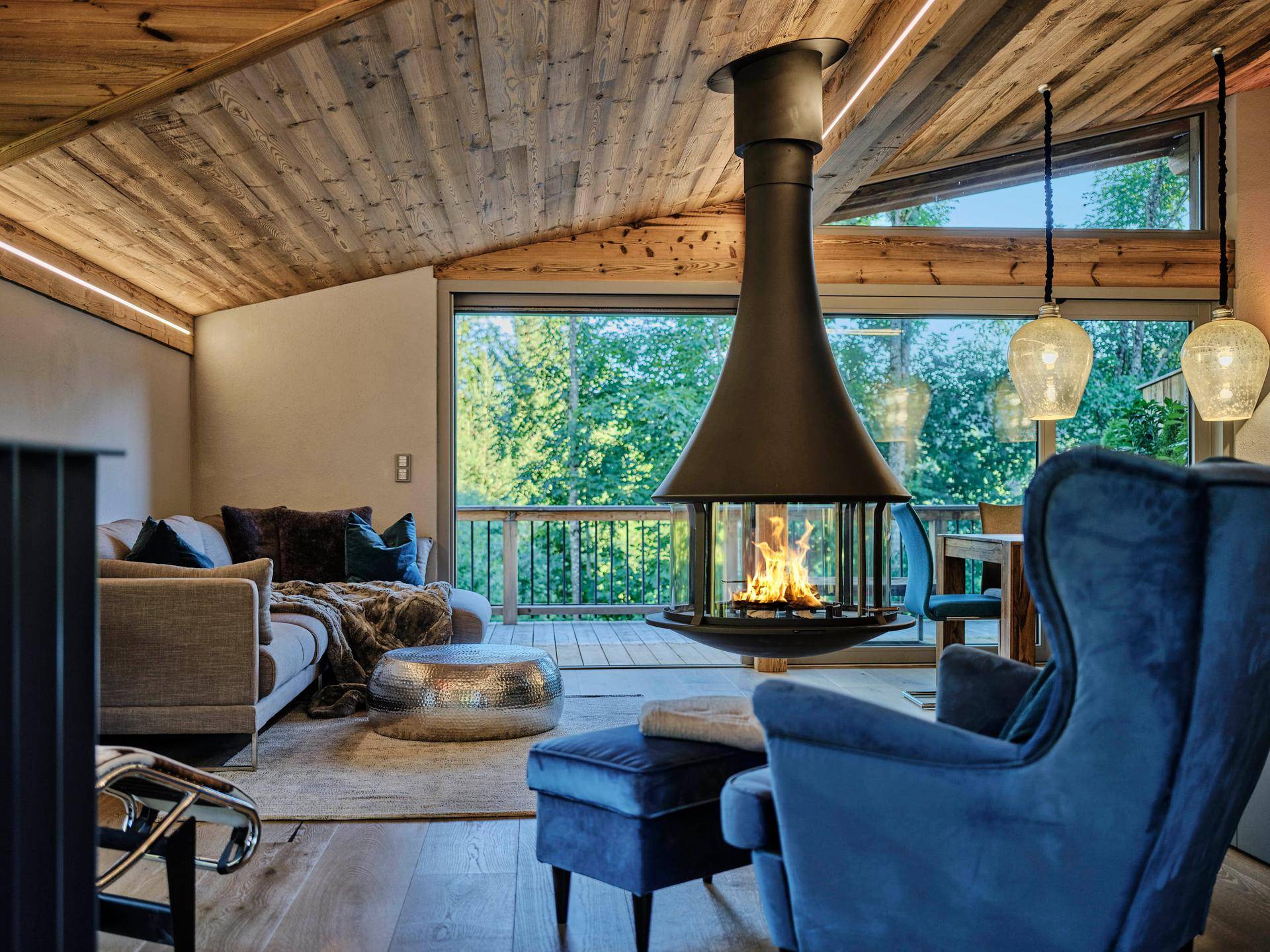 Helles Wohnzimmer mit freistehendem Kamin, bequemen Sofas und weitem Blick ins Grüne.