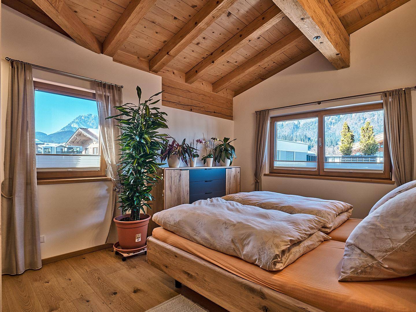 Schlafzimmer mit Holzbalkendecke, Holzboden und Fenstern, die einen schönen Bergblick bieten.