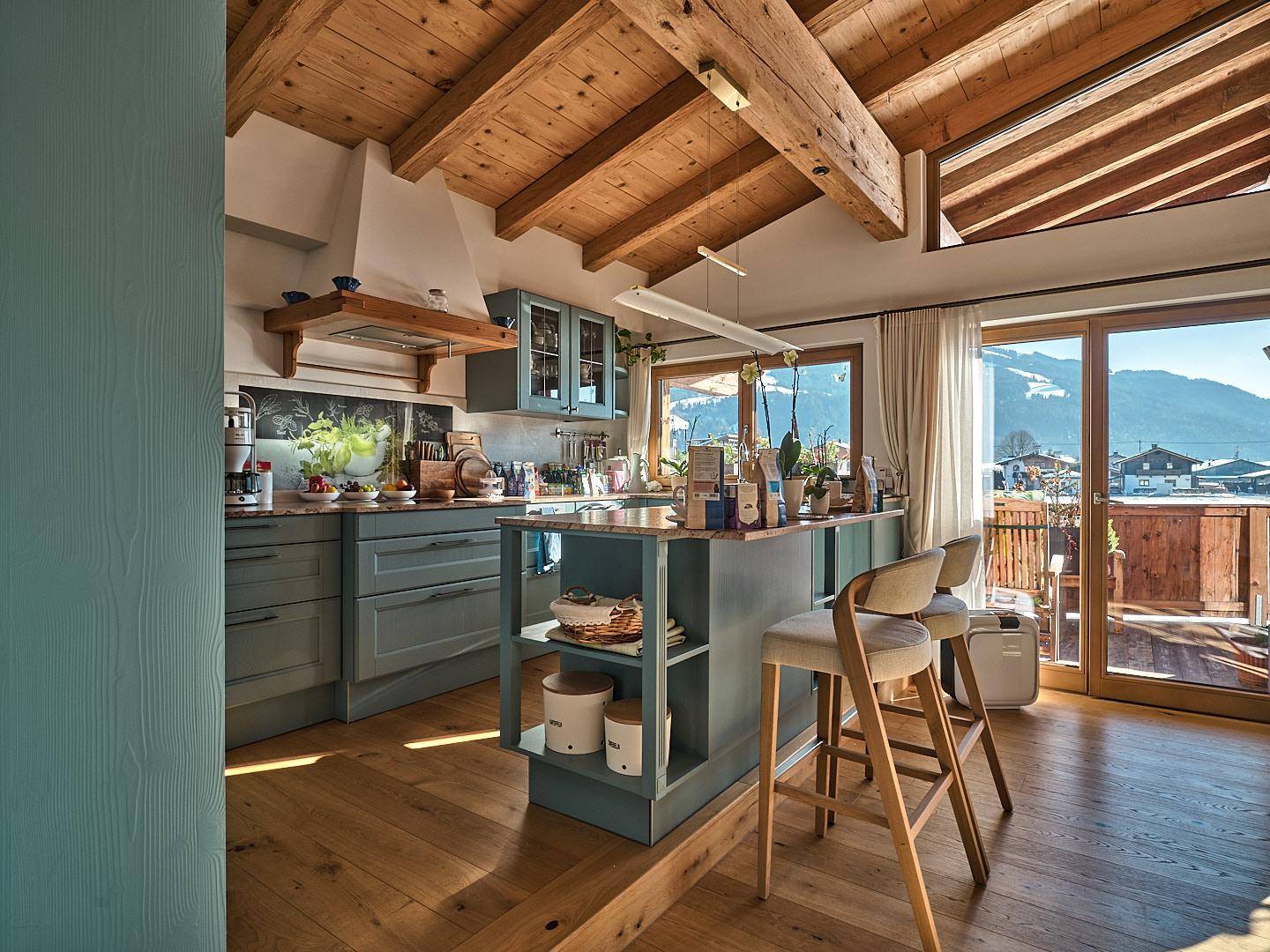 Moderne Küche mit blauen Schränken, Kücheninsel und Zugang zum Balkon mit Bergblick.