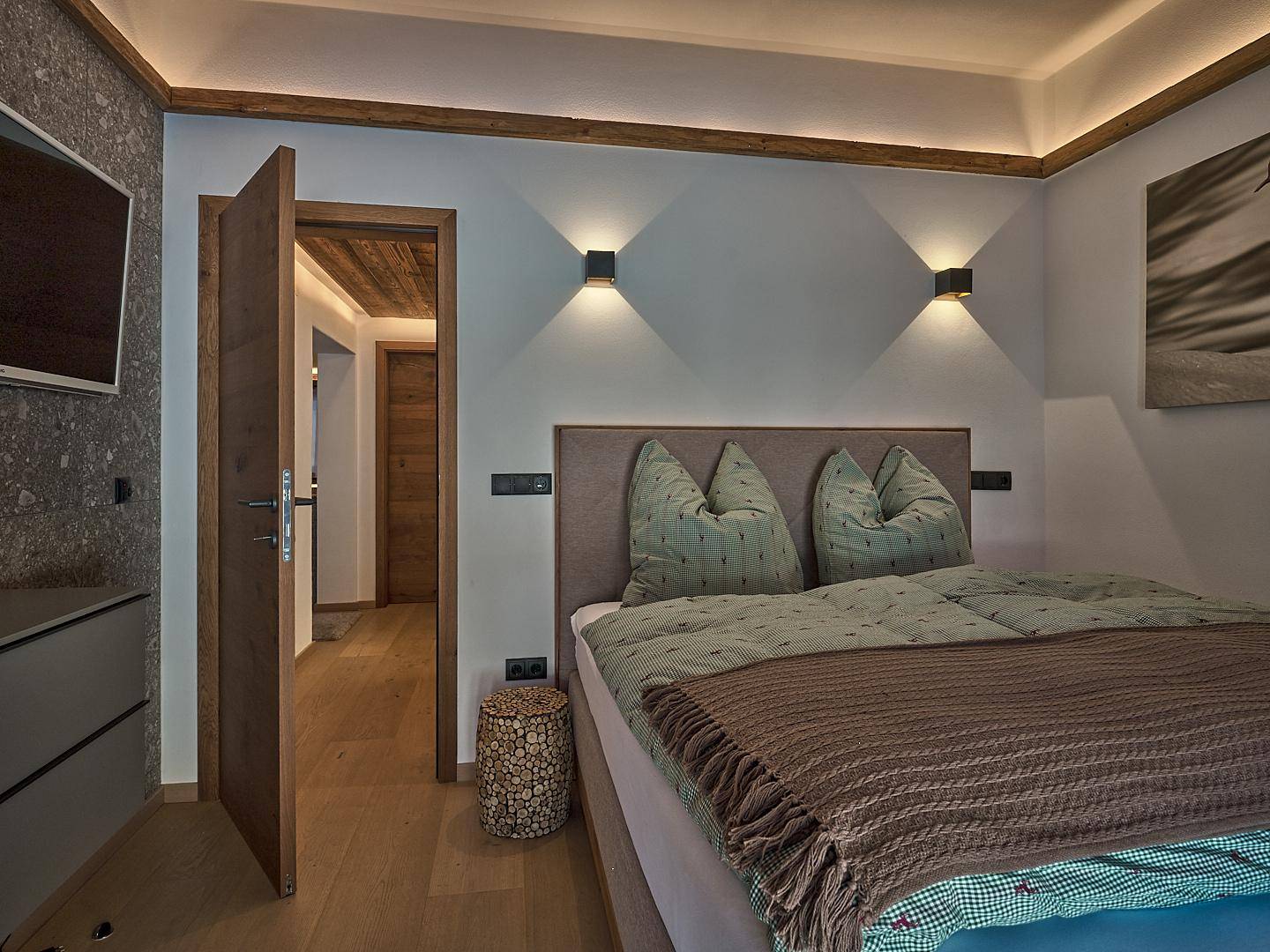 Stilvolles Schlafzimmer mit Holzboden, indirekter Beleuchtung und modernen Wandleuchten.
