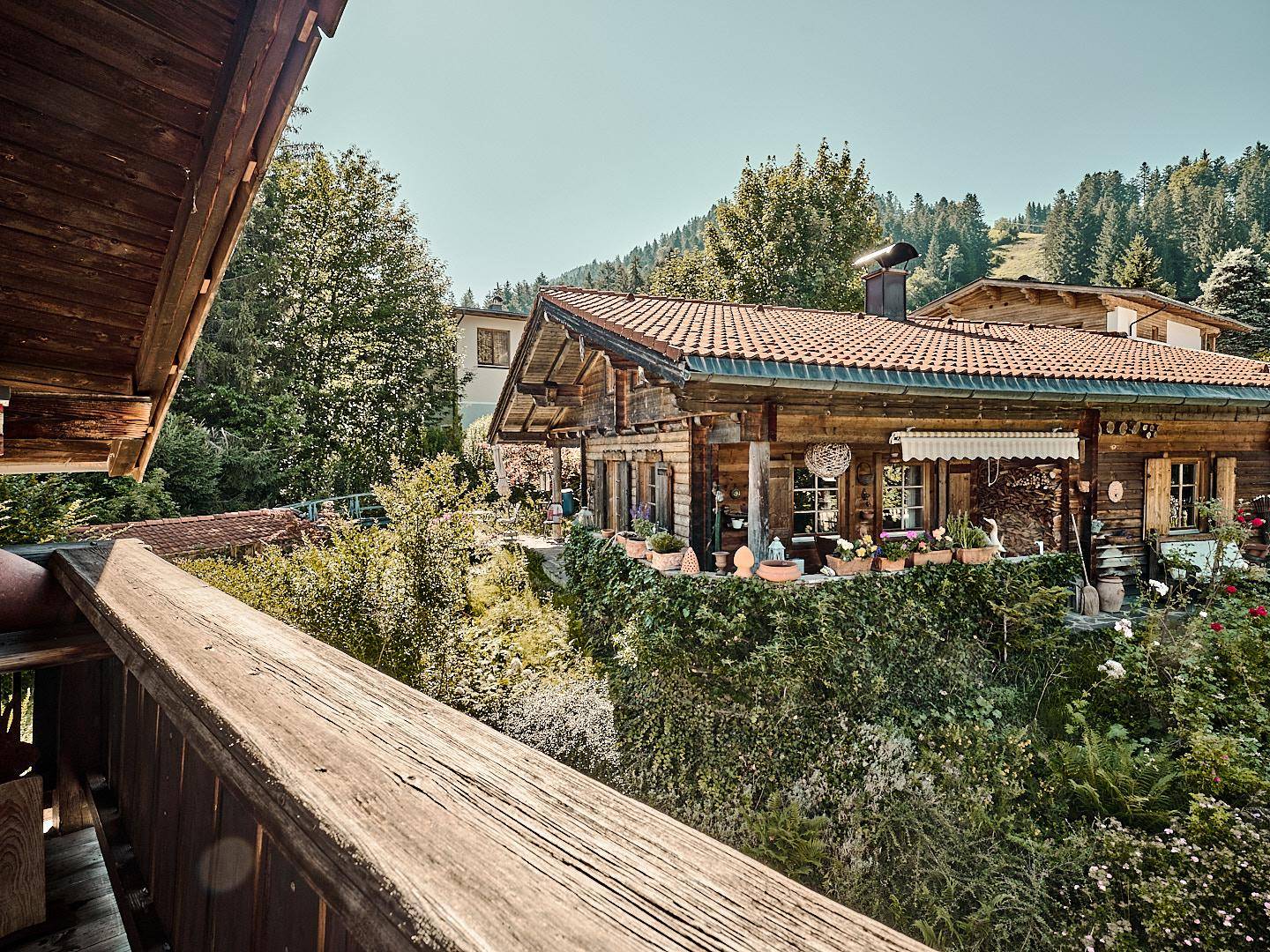 Rustikales Holzhaus mit Terrasse und üppigem Garten, von einem Balkon aus fotografiert.