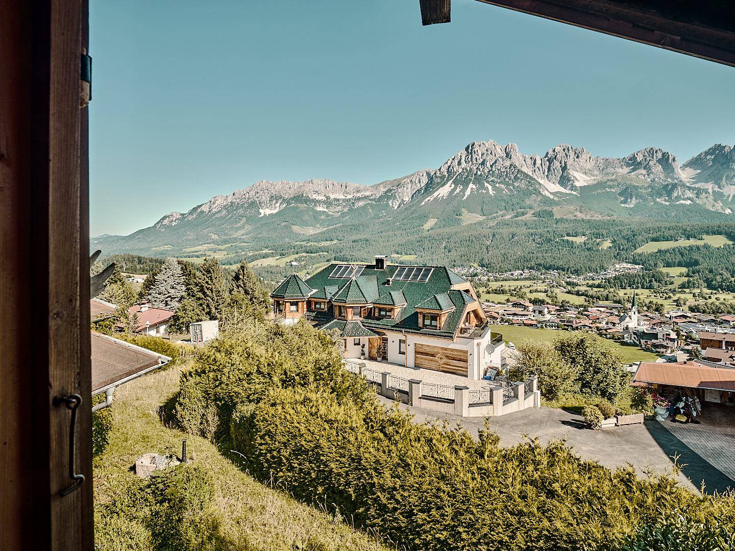 Panoramablick auf ein modernes Haus mit grünem Dach und Solaranlage, umgeben von einem malerischen Tal und Bergen.