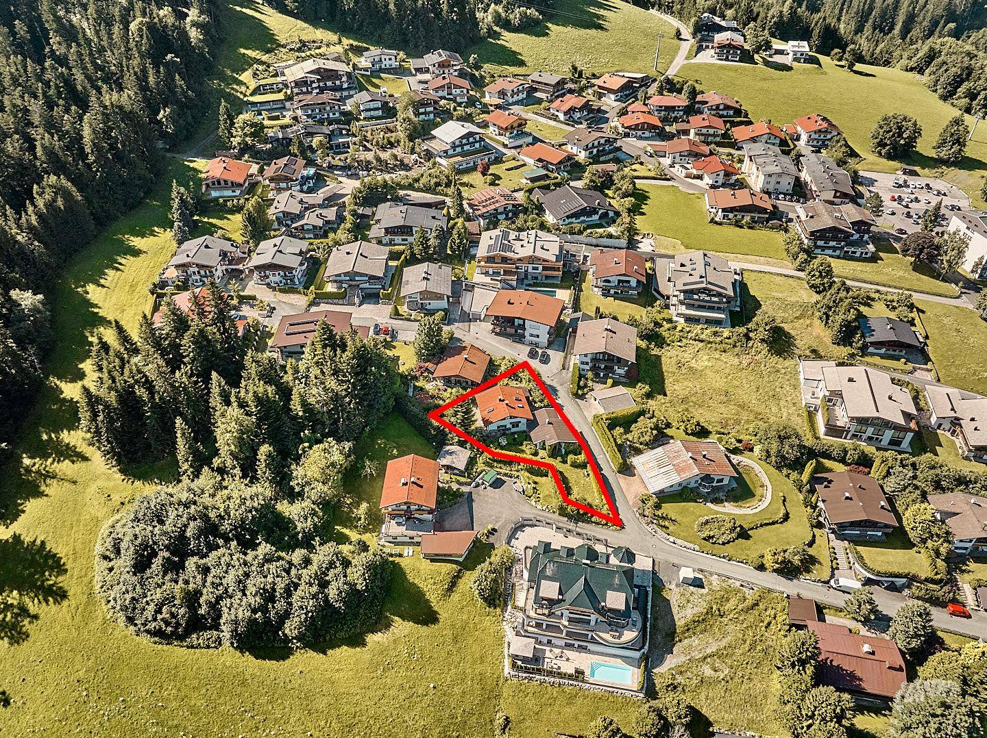 Luftaufnahme eines Wohngebiets mit vielen Häusern und grünen Hügeln, das zum Verkauf stehende Objekt ist rot umrandet.