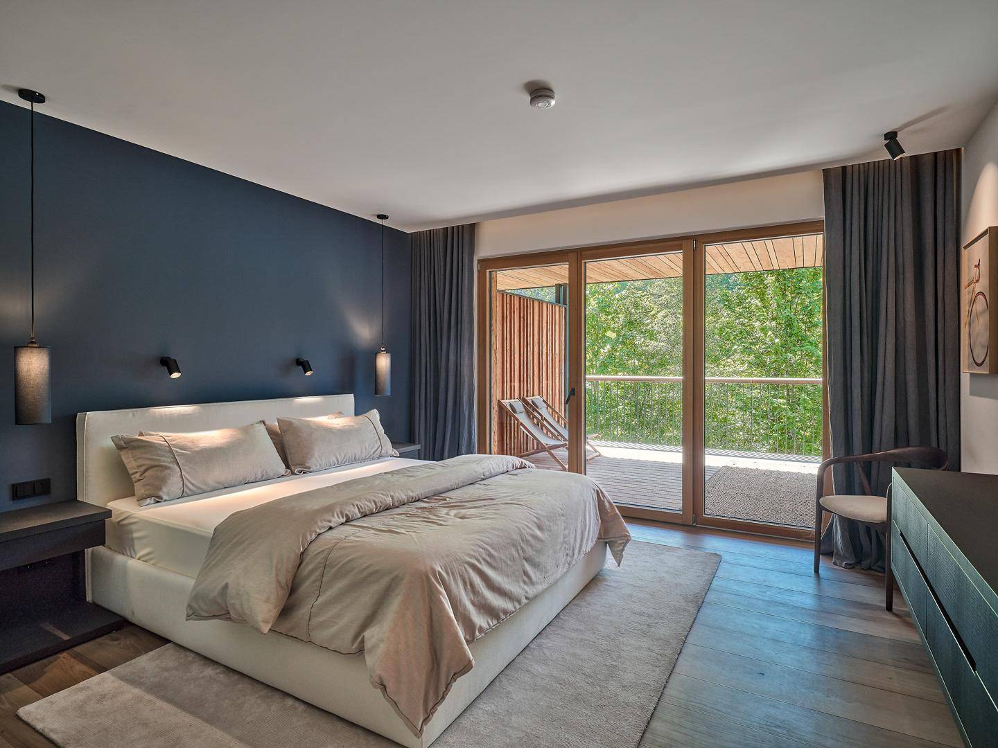 Modernes Schlafzimmer mit großem Bett, blauer Akzentwand und Zugang zum Balkon.