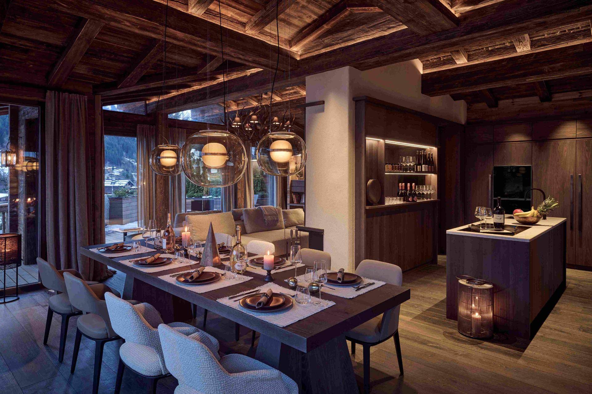 Eleganter Essbereich mit moderner Beleuchtung, offener Küche und Bergblick im luxuriösen Chalet-Stil.