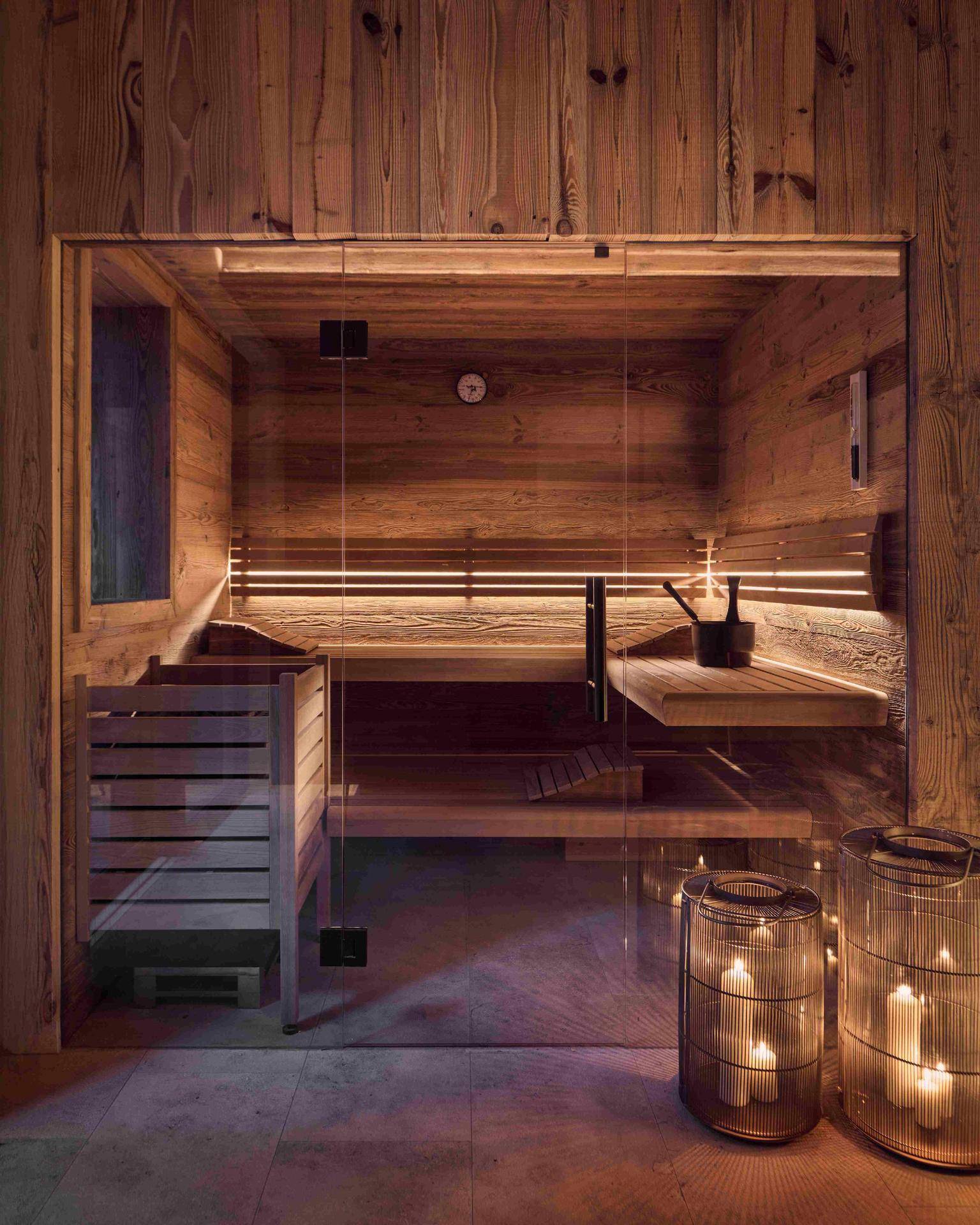 Moderne Holzsauna mit Glasfront, integrierter Beleuchtung und stimmungsvollen Laternen.