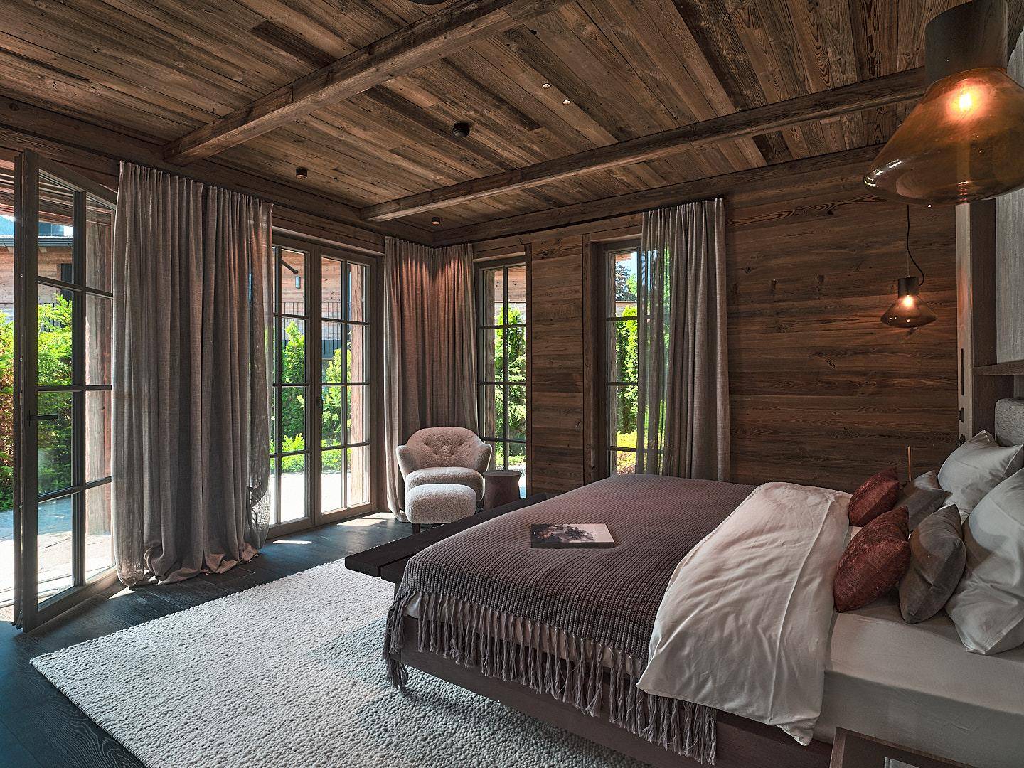 Gemütliches Schlafzimmer im alpinen Stil mit Holzwänden, hohen Decken und Zugang zu einem Außenbereich durch Fenstertüren.