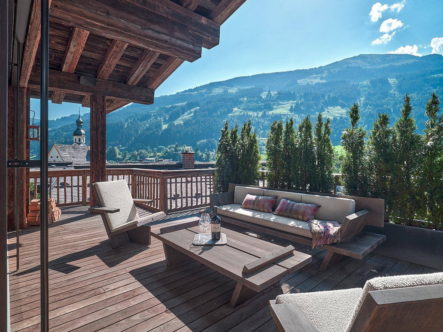 Große Holzterrasse mit bequemen Outdoor-Möbeln und einem atemberaubenden Blick auf die Berge und das Tal.