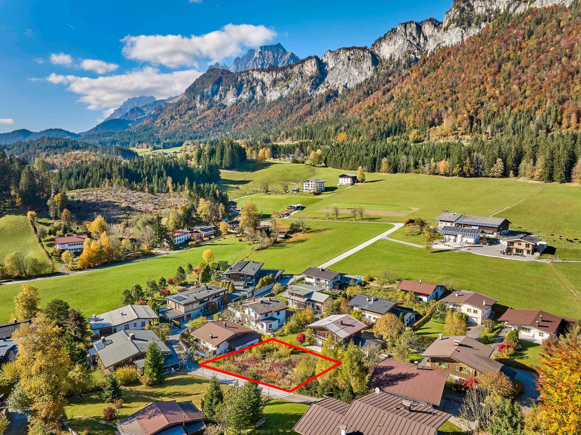 Luftaufnahme eines Baugrundstücks in einer malerischen Berglandschaft mit umliegenden Häusern.