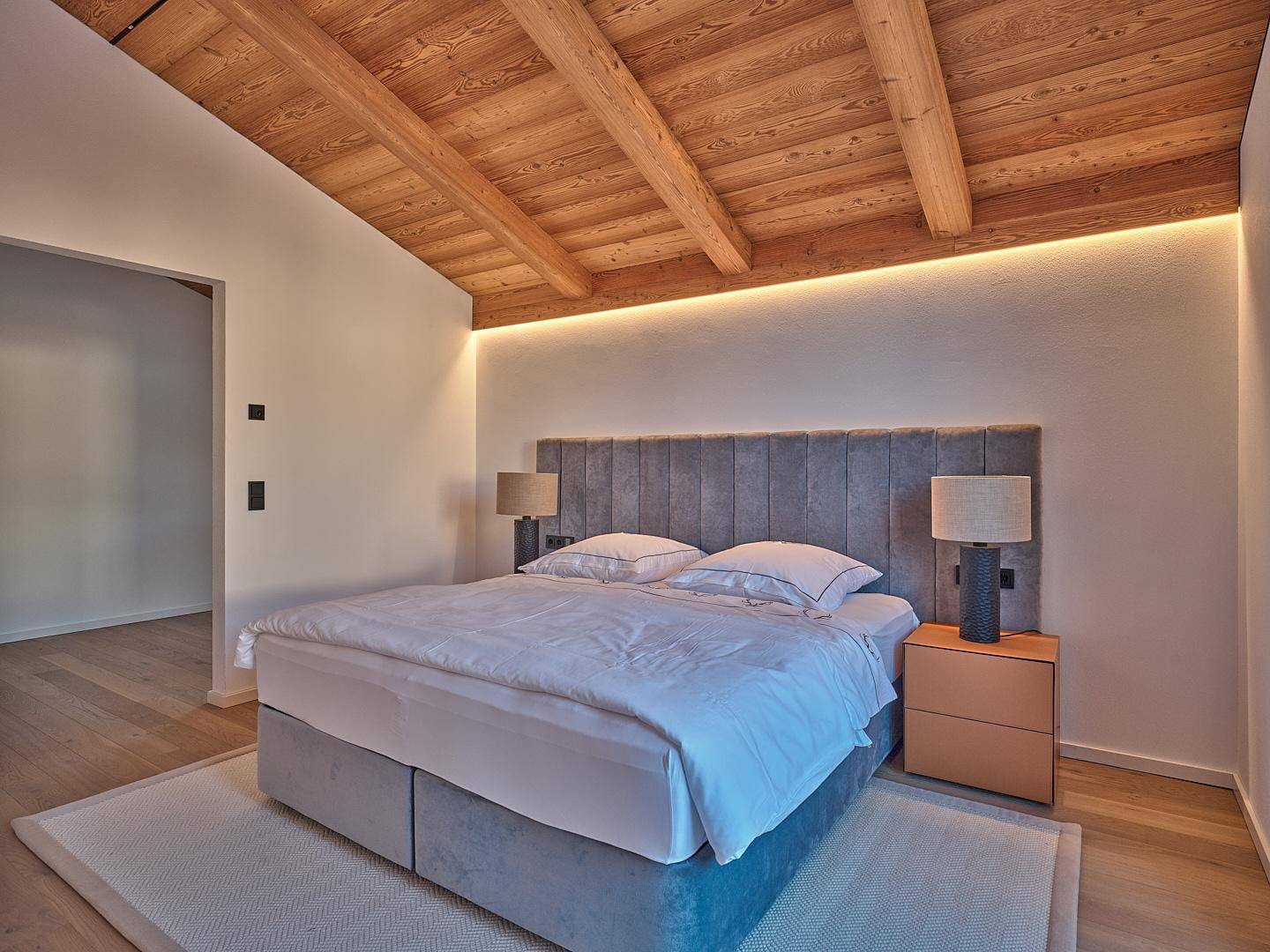 Gemütliches Schlafzimmer mit Holzbalkendecke, indirekter Beleuchtung und modernem Bett.
