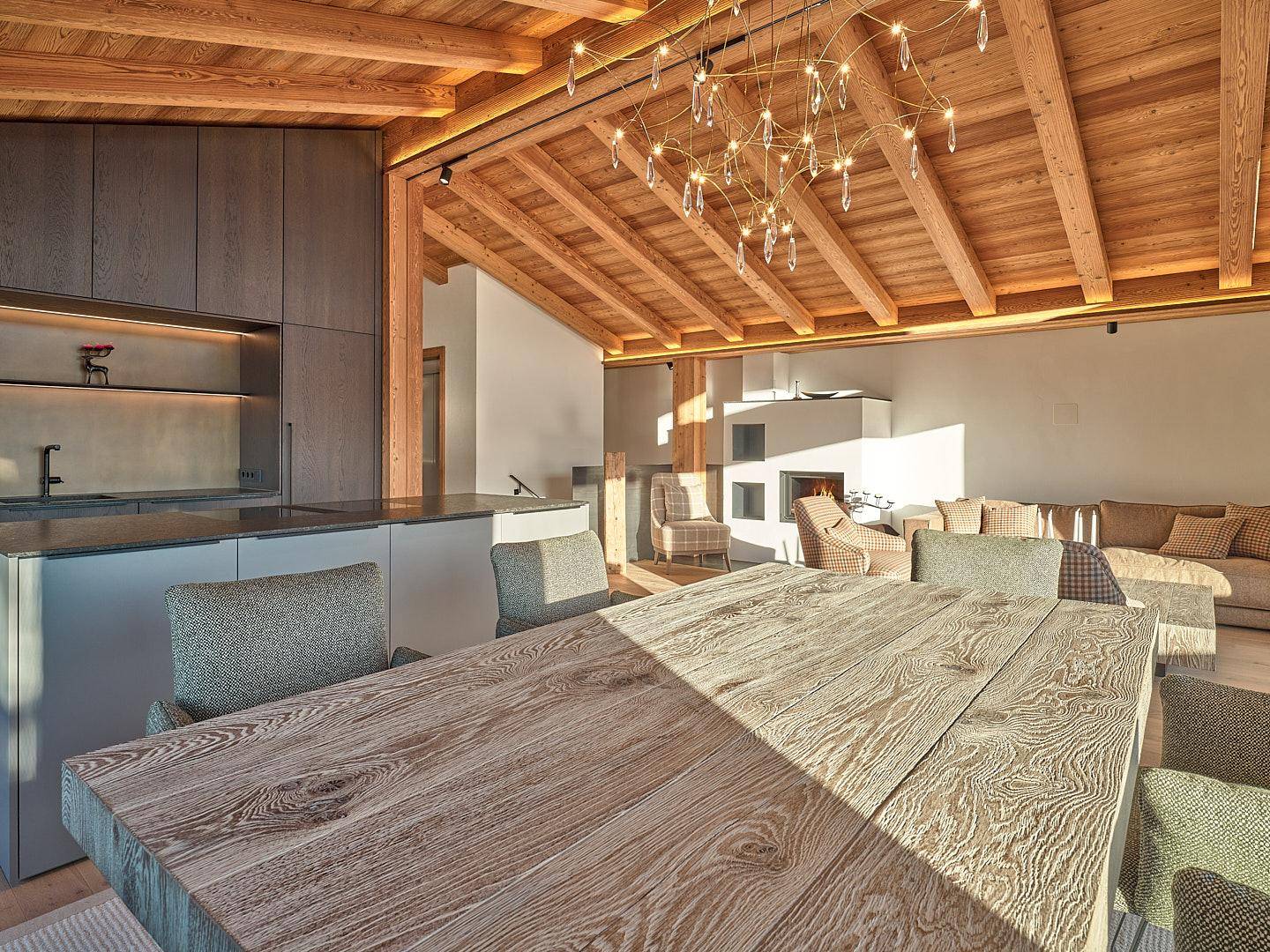 Heller offener Wohn-Essbereich mit Holzbalkendecke, modernem Kronleuchter und Kamin.