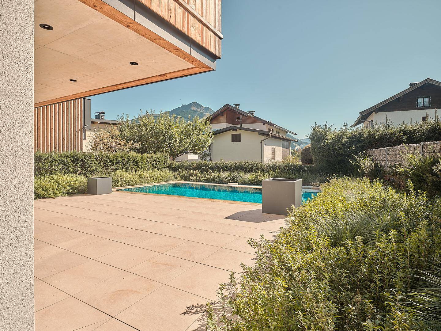 Sonniger Terrassenbereich mit Pool, umgeben von Grünflächen und Blick auf die Berge.