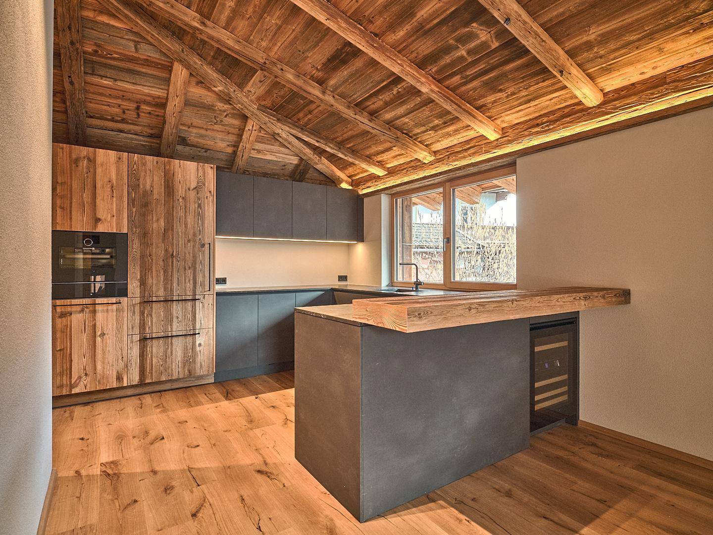 Moderne Küche mit Holzelementen, dunklen Unterschränken und einer Kücheninsel mit Frühstücksbar.