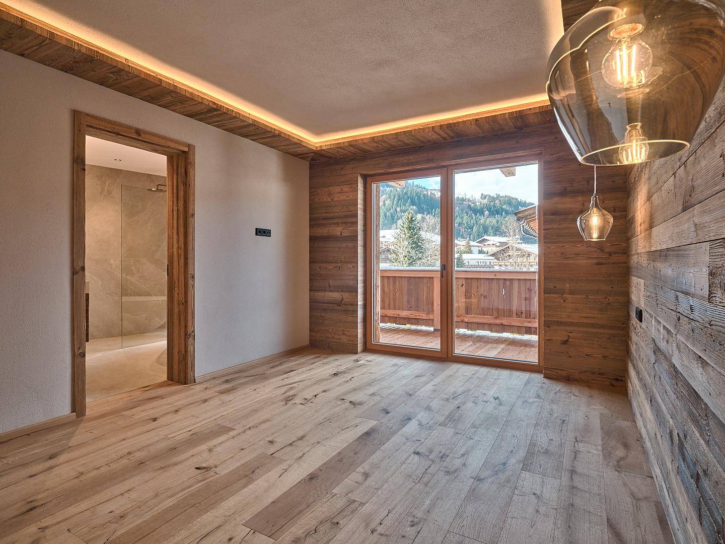 Gemütliches Schlafzimmer mit Holzwänden, Parkettboden und Zugang zu einem Balkon mit Bergblick.