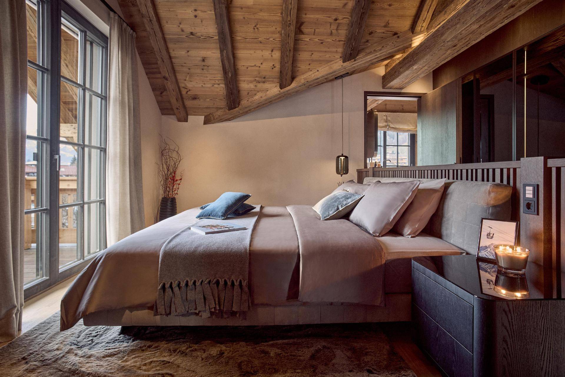 Elegantes Schlafzimmer mit großem Bett, Holzbalkendecke und direktem Zugang zum Balkon.