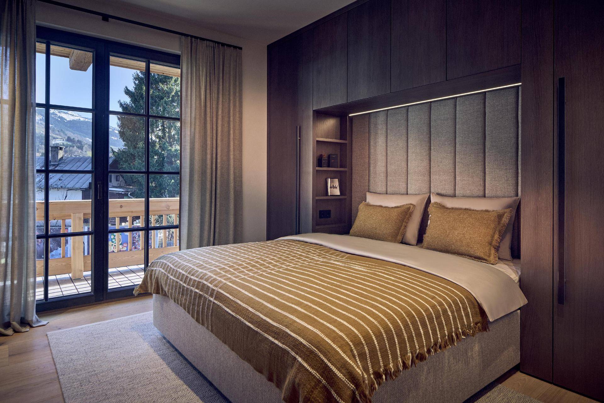 Gemütliches Schlafzimmer mit Einbauschränken, Balkonzugang und Blick auf die Berglandschaft.