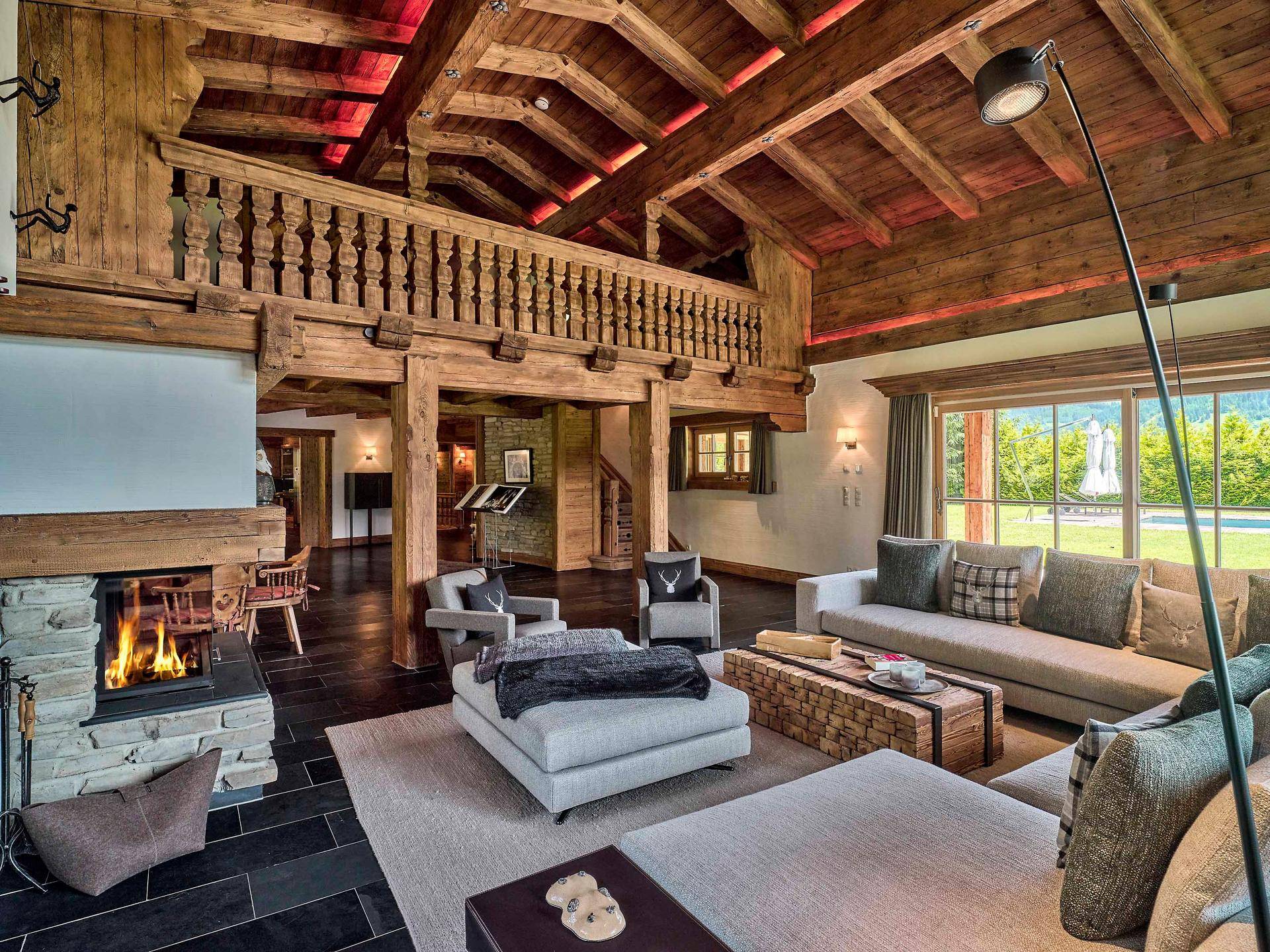 Gemütliches Wohnzimmer im Chalet-Stil mit Kamin, Holzbalken und Blick ins Grüne.