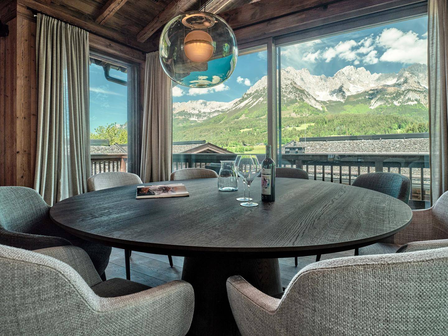 Eleganter Essbereich mit großem Holztisch und atemberaubendem Bergblick durch Panoramafenster.