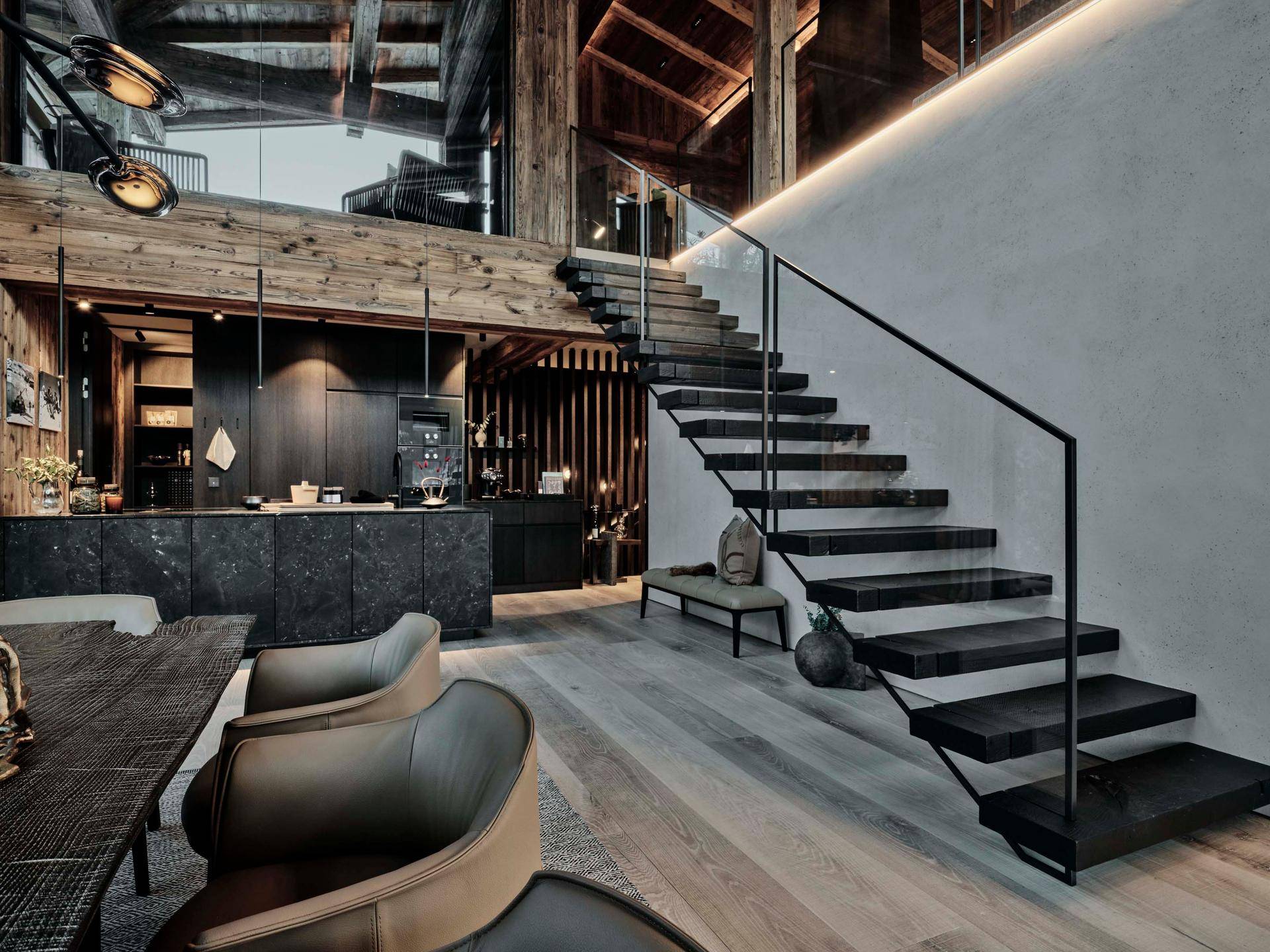 Elegante moderne Treppe mit Glasgeländer in einem offenen Wohnbereich mit dunkler Küche im Hintergrund.