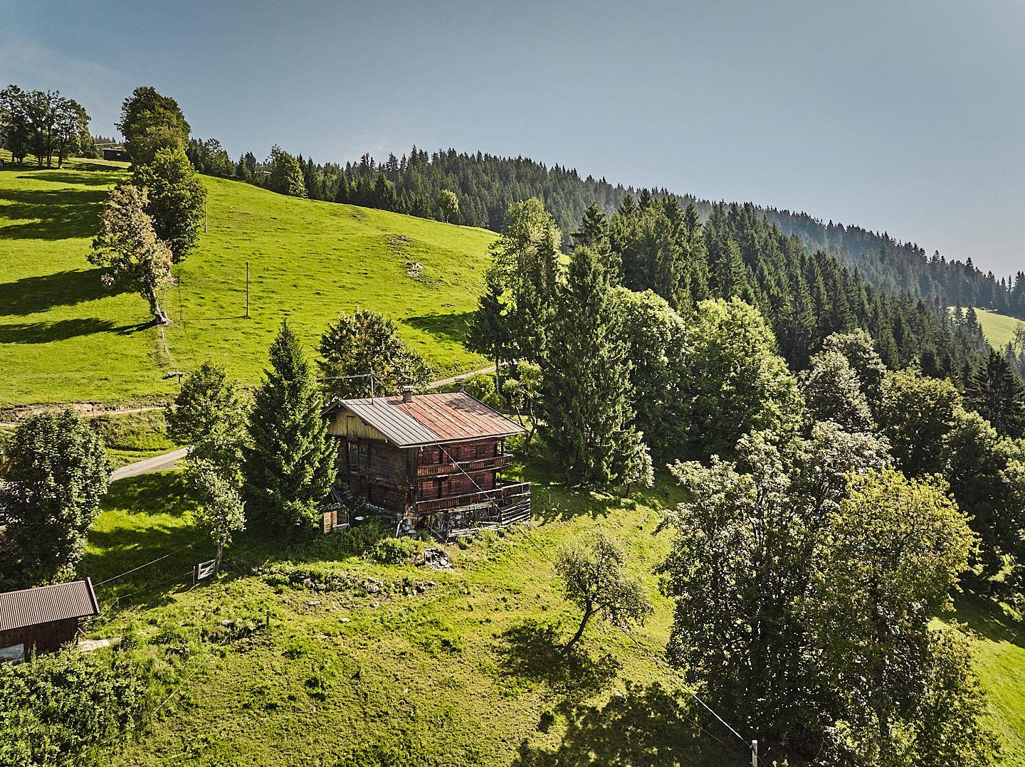 Malerisches Holzhaus eingebettet in eine grüne Hügellandschaft mit Wäldern und Wegen.