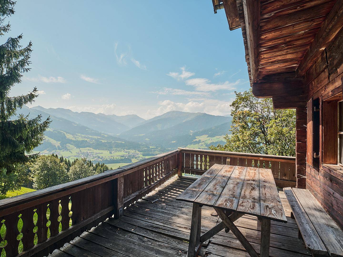 Geräumige Holzterrasse mit rustikalen Möbeln und weitem Blick über das Tal und die Berge.