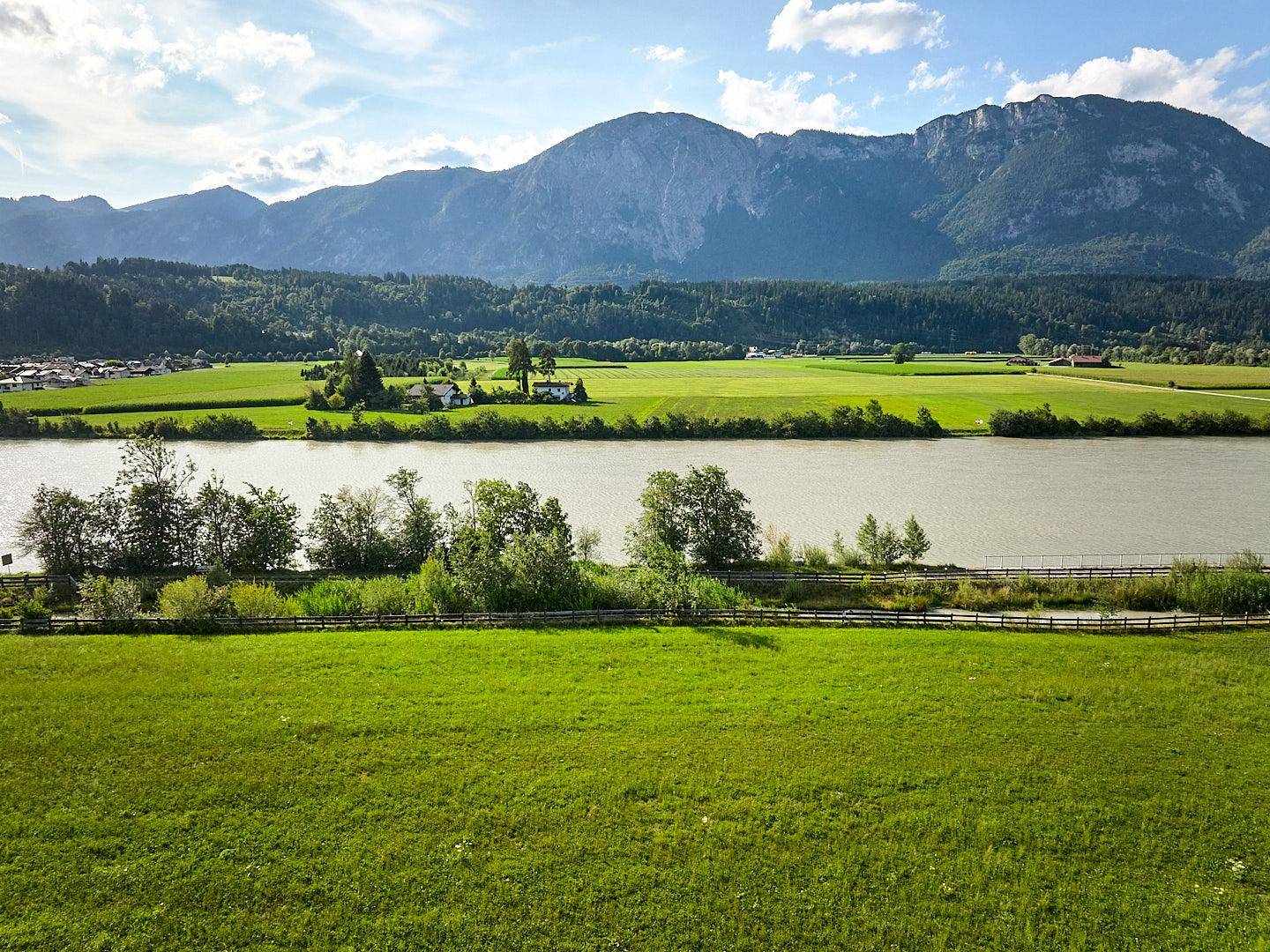 Weitläufige grüne Landschaft mit einem Fluss, umgeben von Bergen unter blauem Himmel.