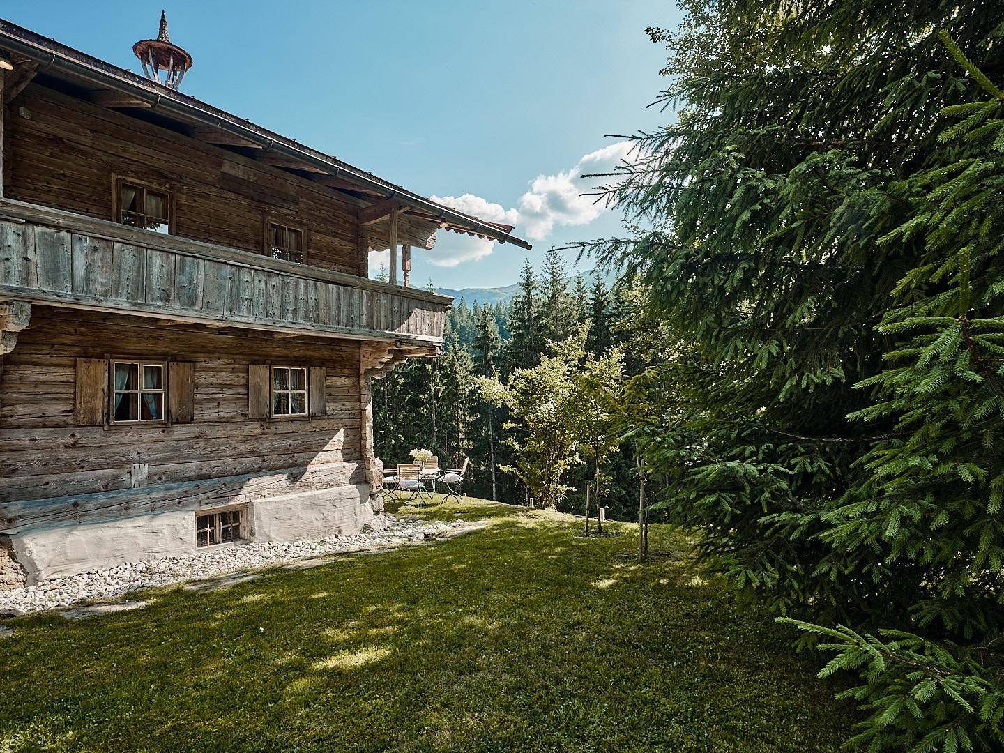 Sonnige Gartenterrasse am Holzchalet mit Sitzgelegenheiten und Blick auf die umliegende Berglandschaft.