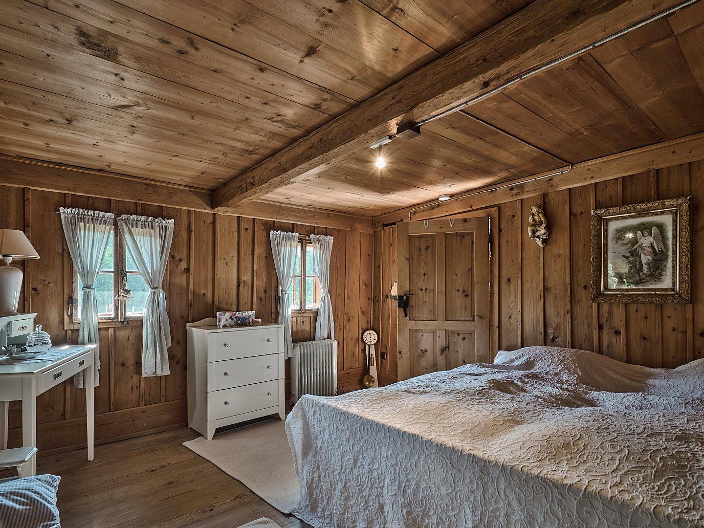 Rustikales Schlafzimmer mit Holztäfelung, Doppelbett und traditionellen Fenstern.