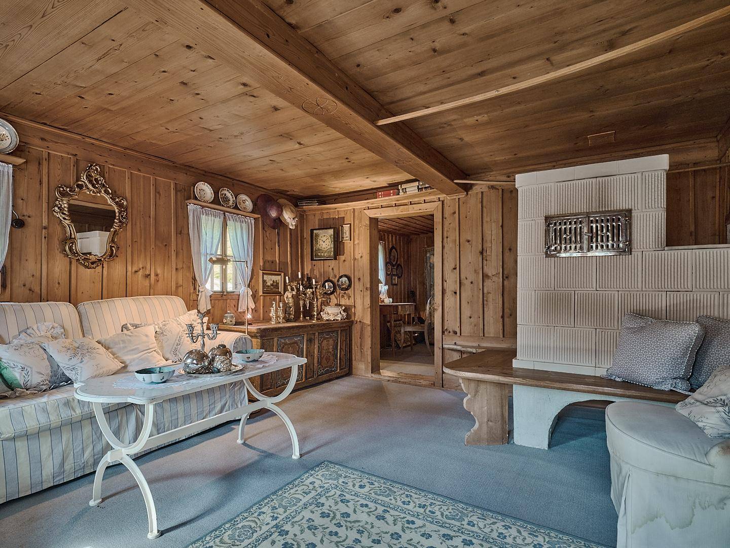 Gemütliches Wohnzimmer im alpinen Stil mit Holztäfelung, Kachelofen und traditionellen Möbeln.