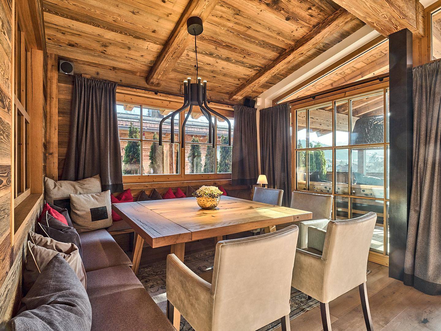 Gemütlicher Essbereich im Chalet-Stil mit Holztisch, Sitzbank und großen Fenstern.